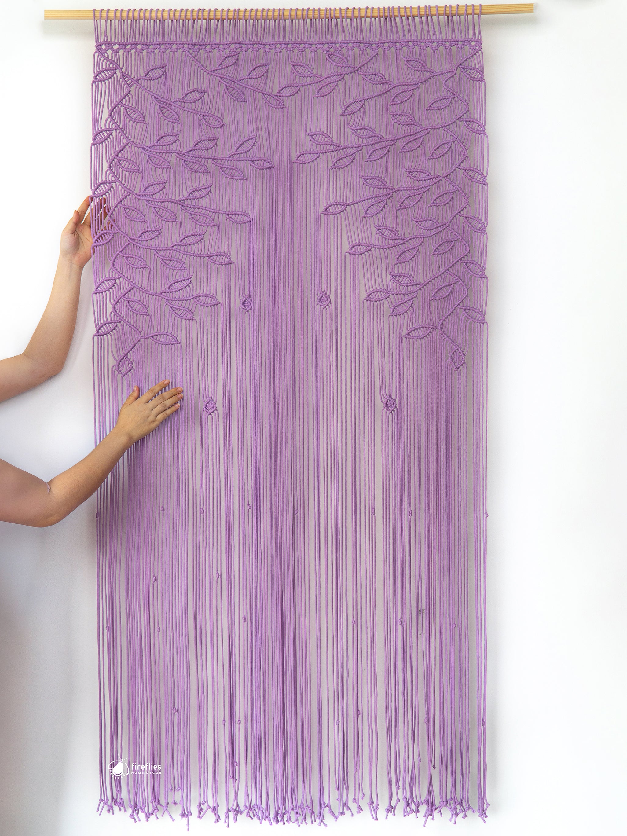 Purple string curtain with leaf pattern held by a person against a white background