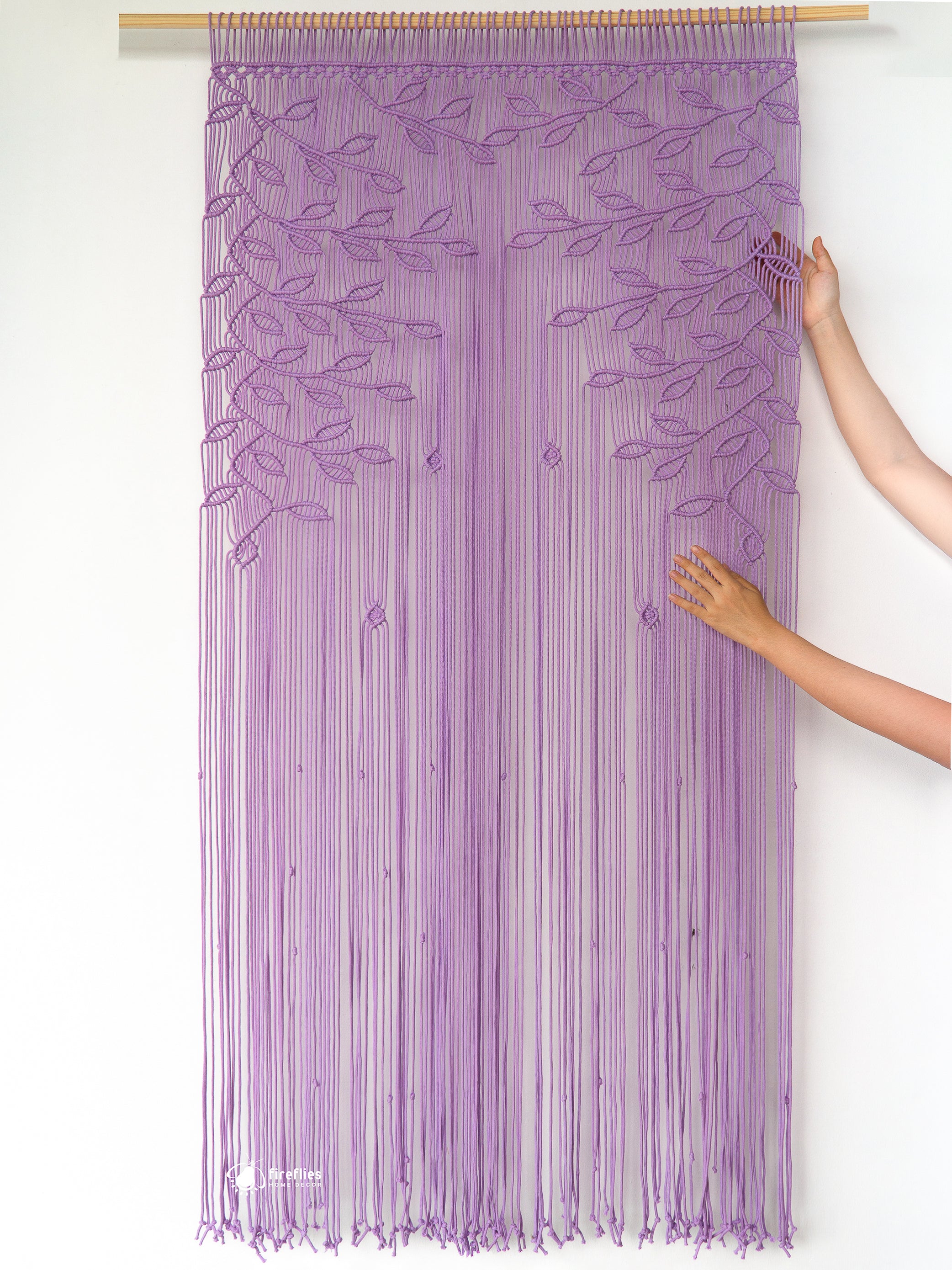 Purple string curtain with leaf pattern being held by a hand on a white background