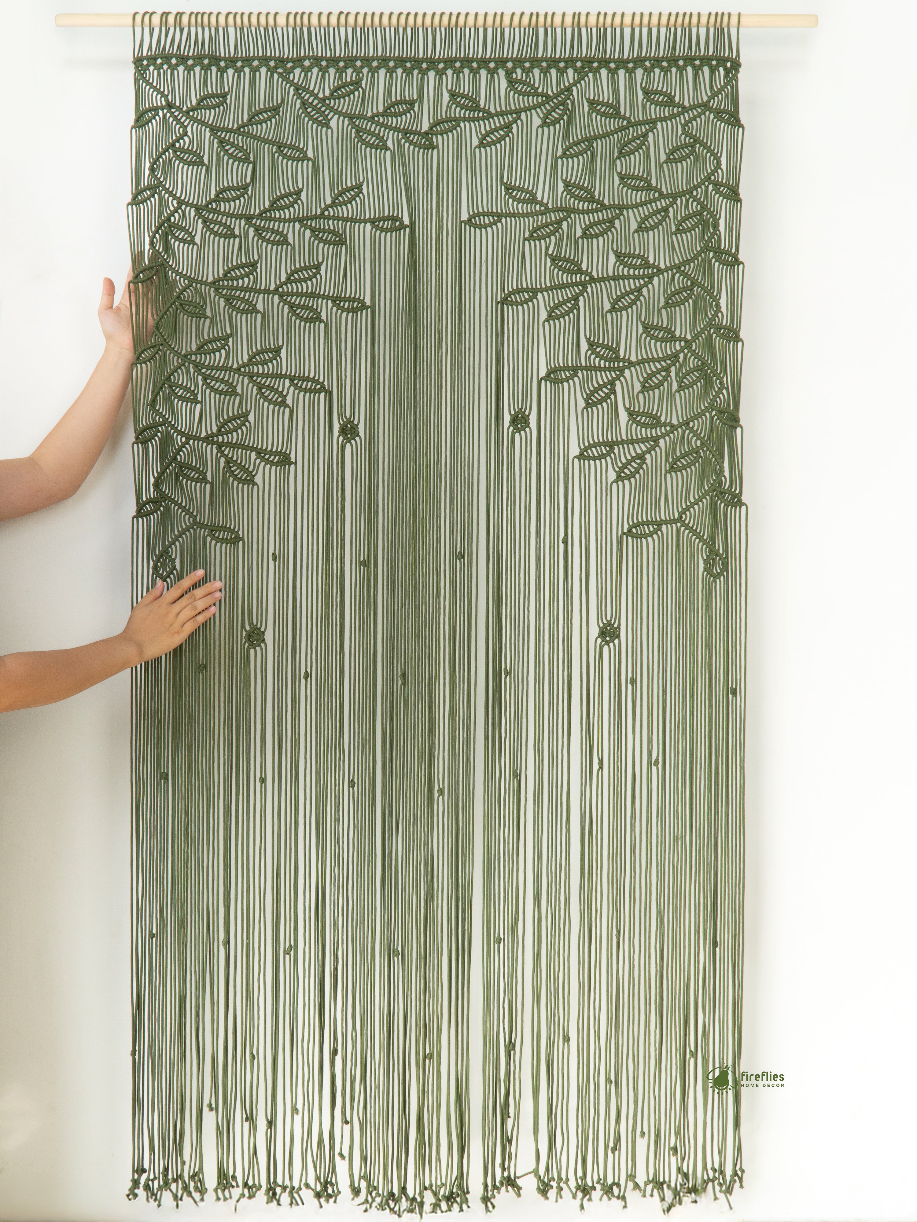 Green string curtain with leaf pattern held up by a person against a white background