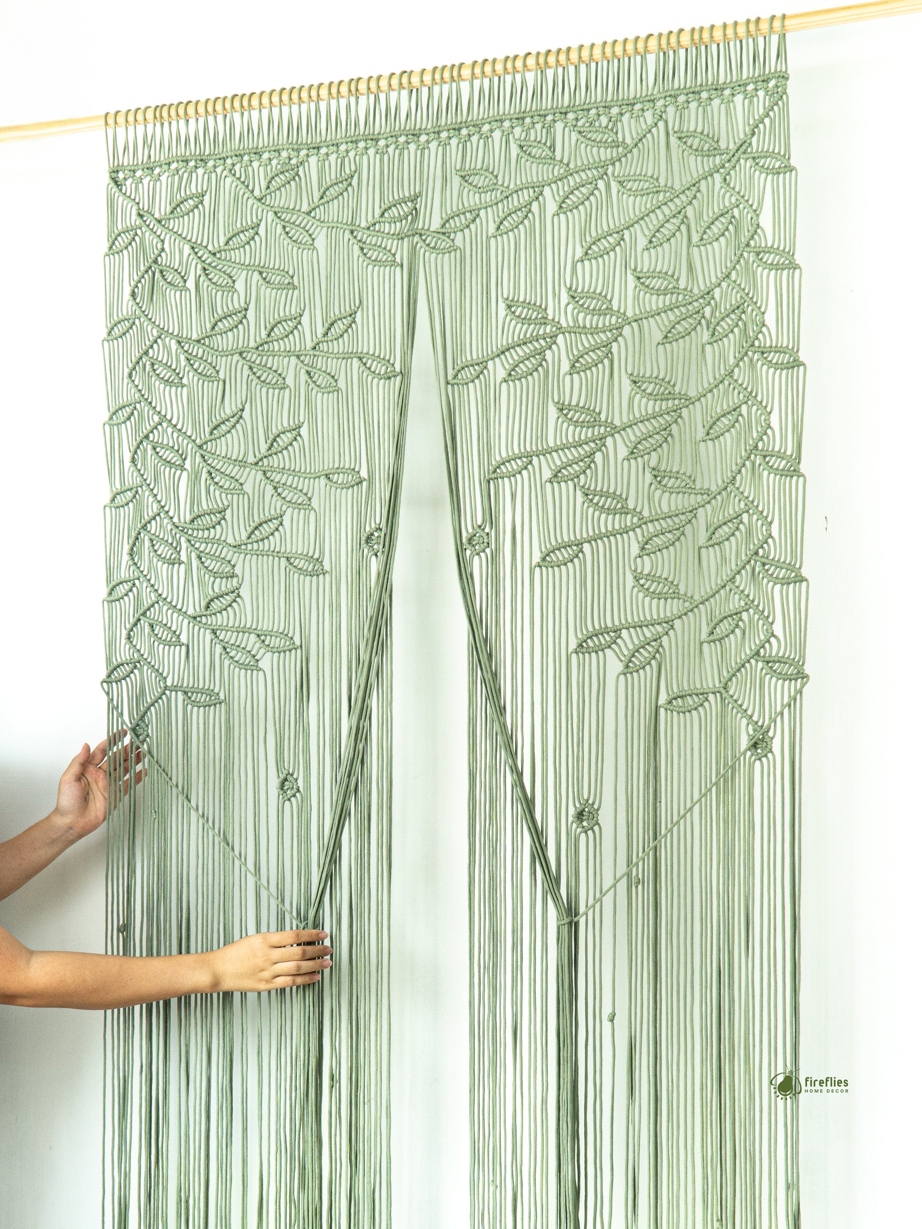 Green leaf-patterned string curtain being held by a person against a white wall.