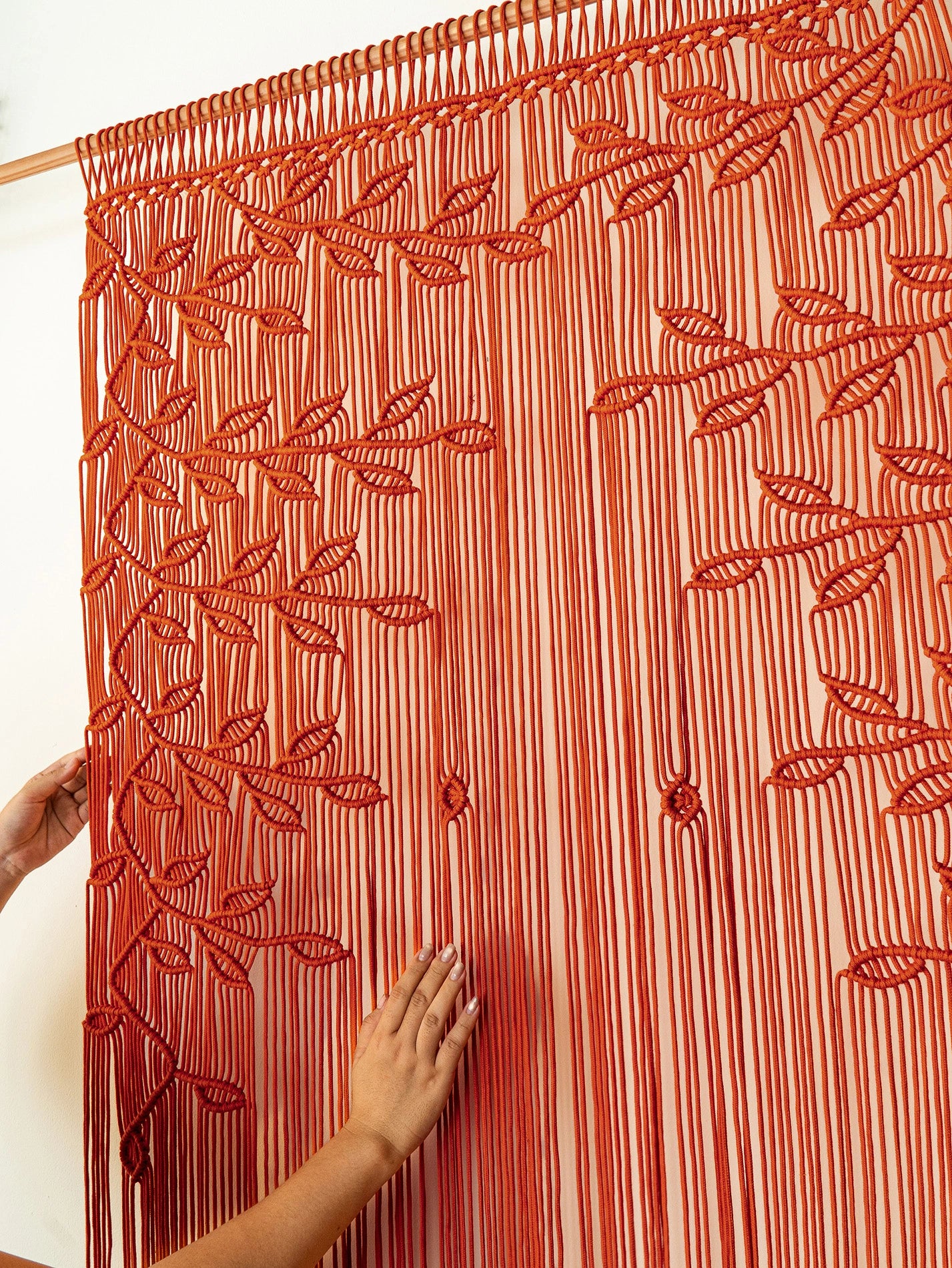A red and white striped curtain panel with embroidered leaf patterns, shown hanging on a wooden rod with hands adjusting it.