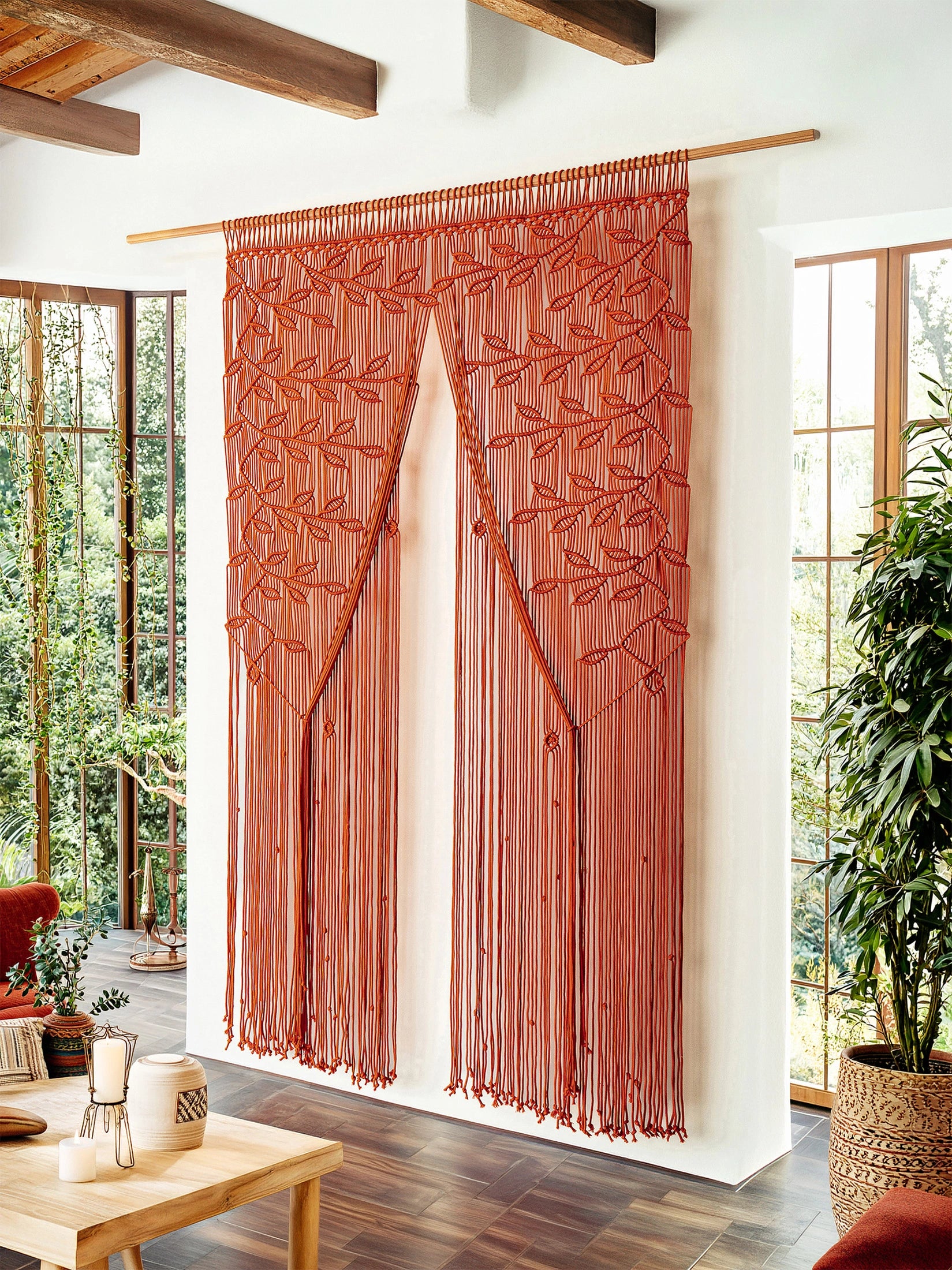 A rust-orange beaded curtain with a leaf pattern hangs from a wooden rod in a bright, modern room with large windows and wood floors.