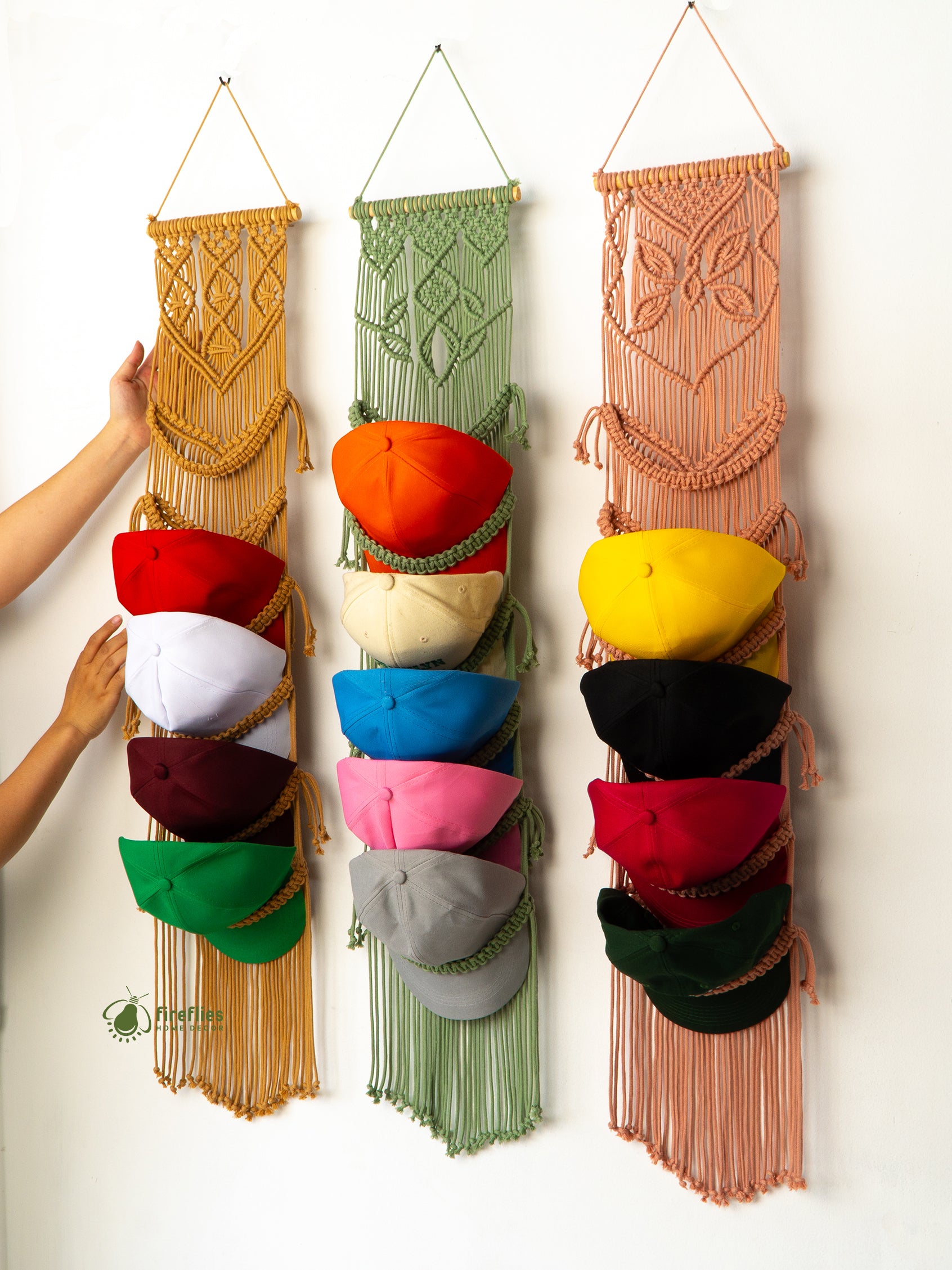 Three colorful macrame hat racks with hats hanging on them against a white background.