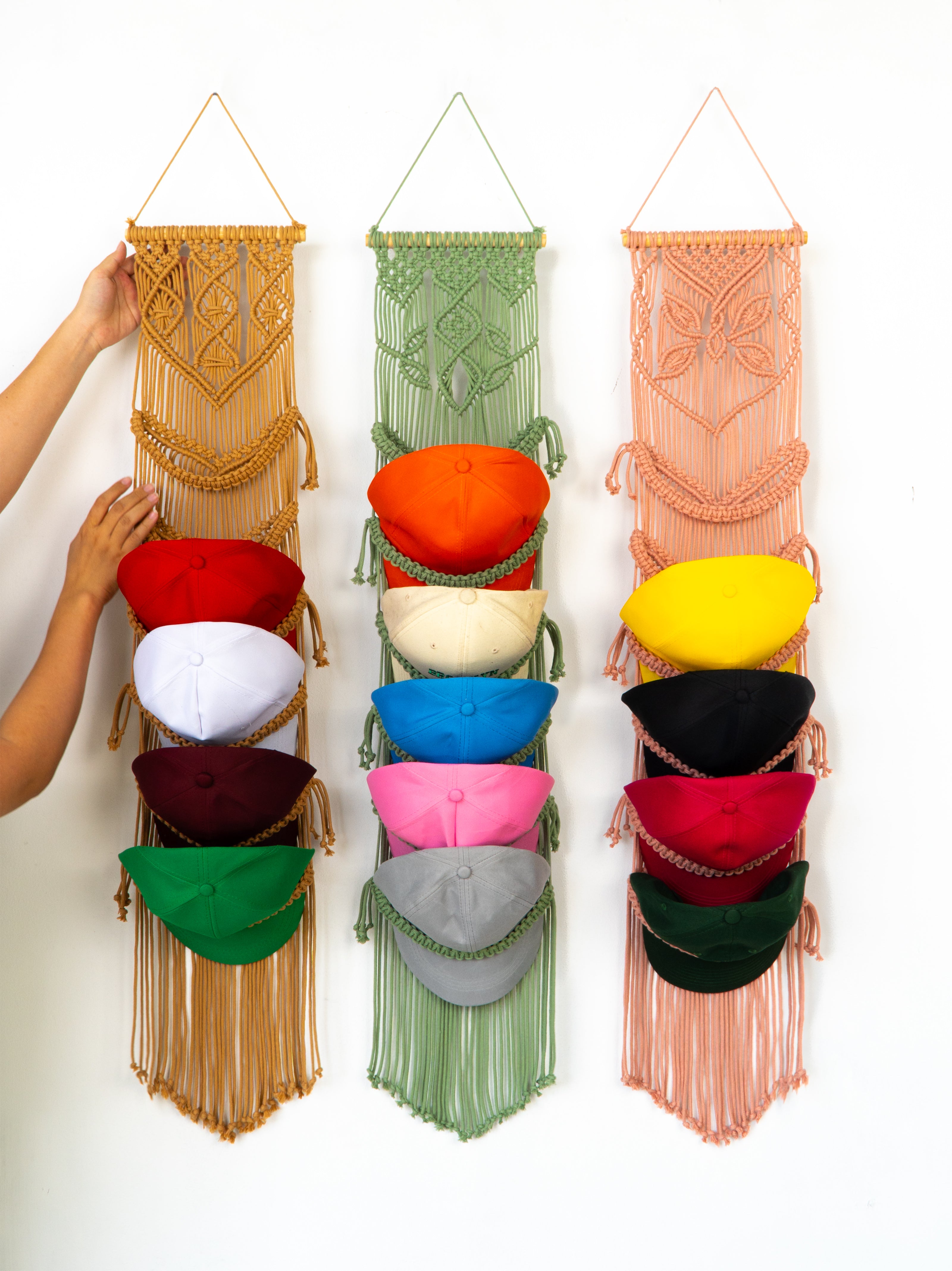Colorful macrame hat rack with various colored hats on a white background