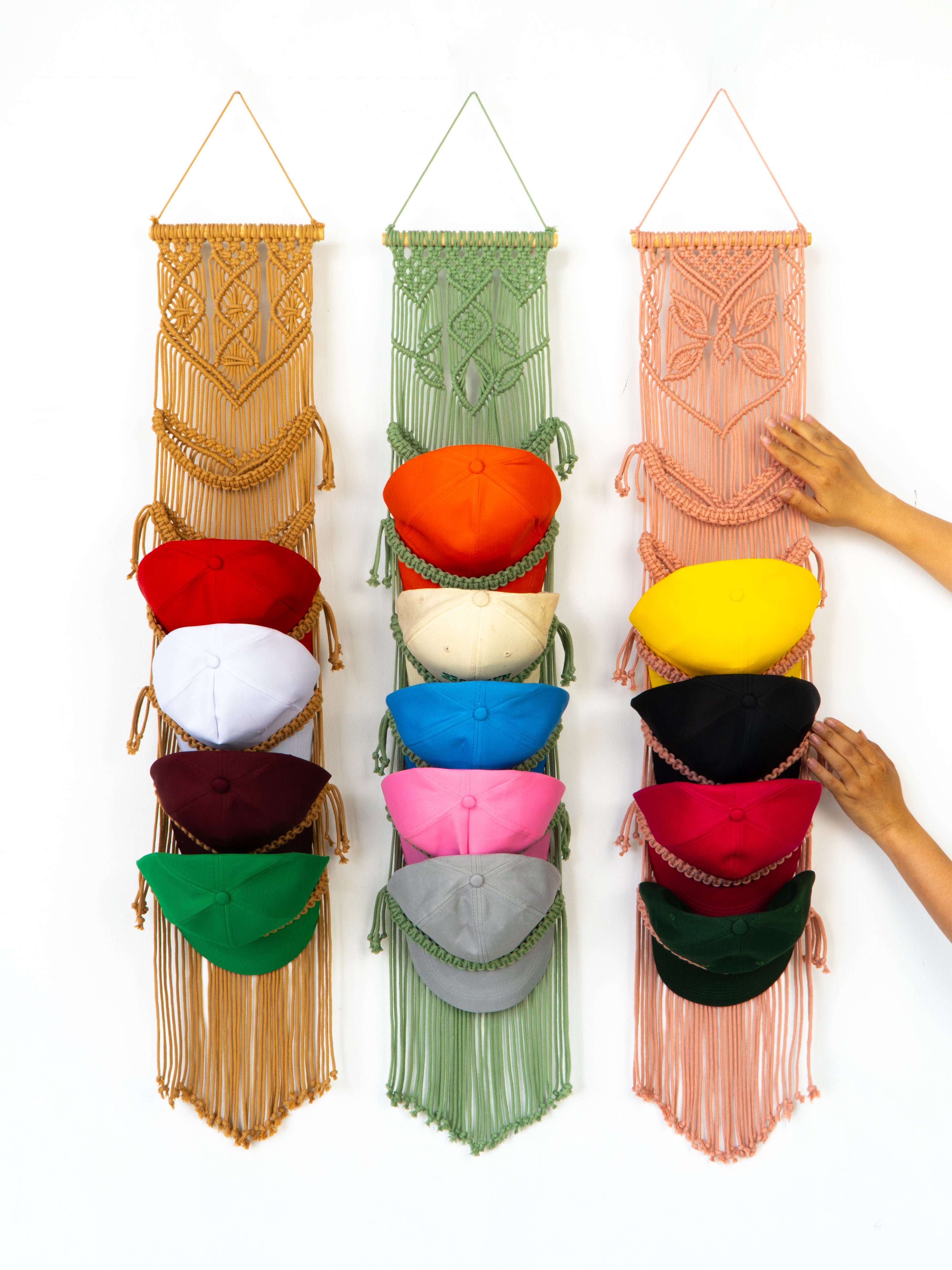 Colorful macrame wall hanging with hats on a white background