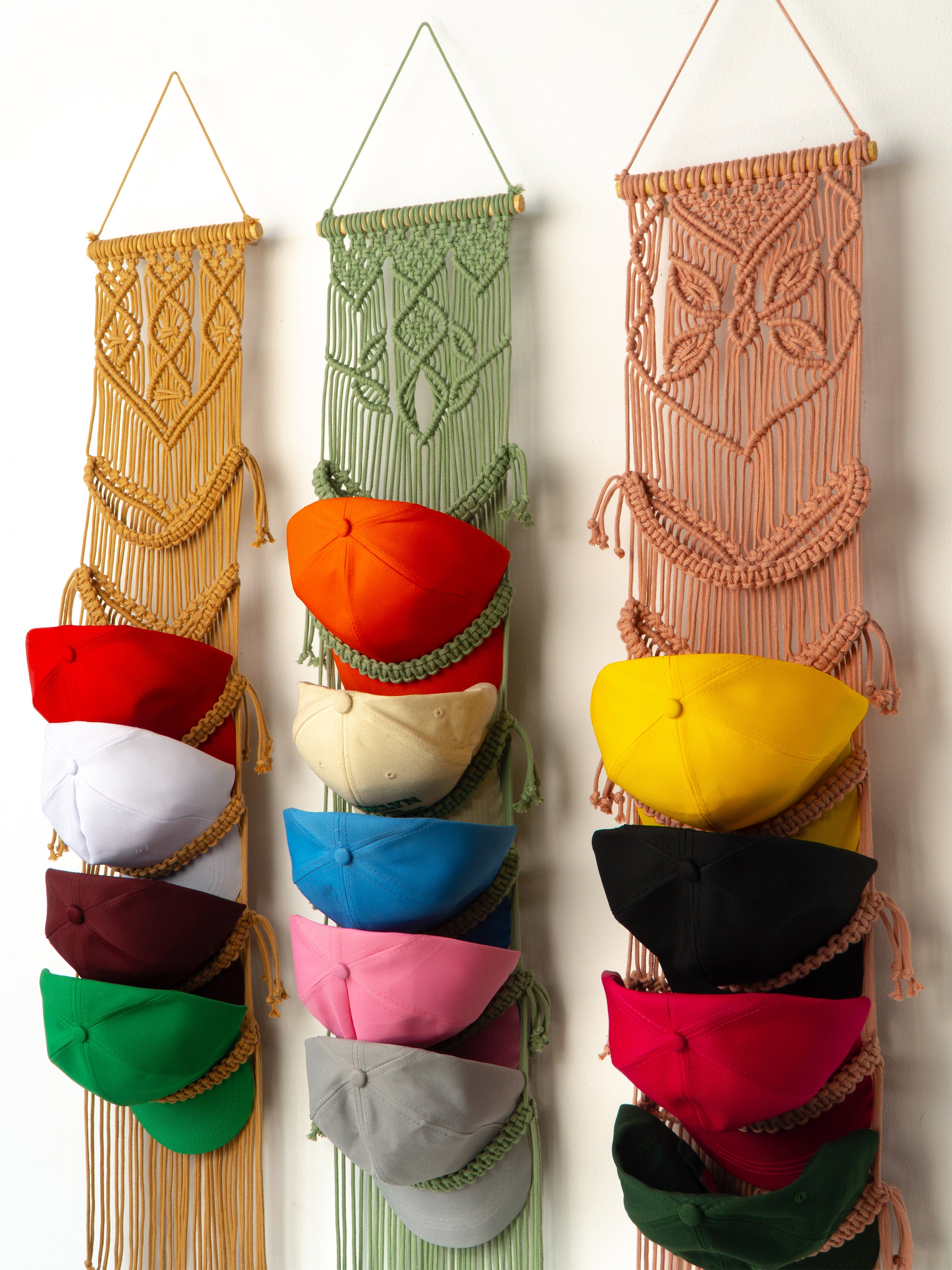 Colorful macrame hat rack with various colored hats on a white wall