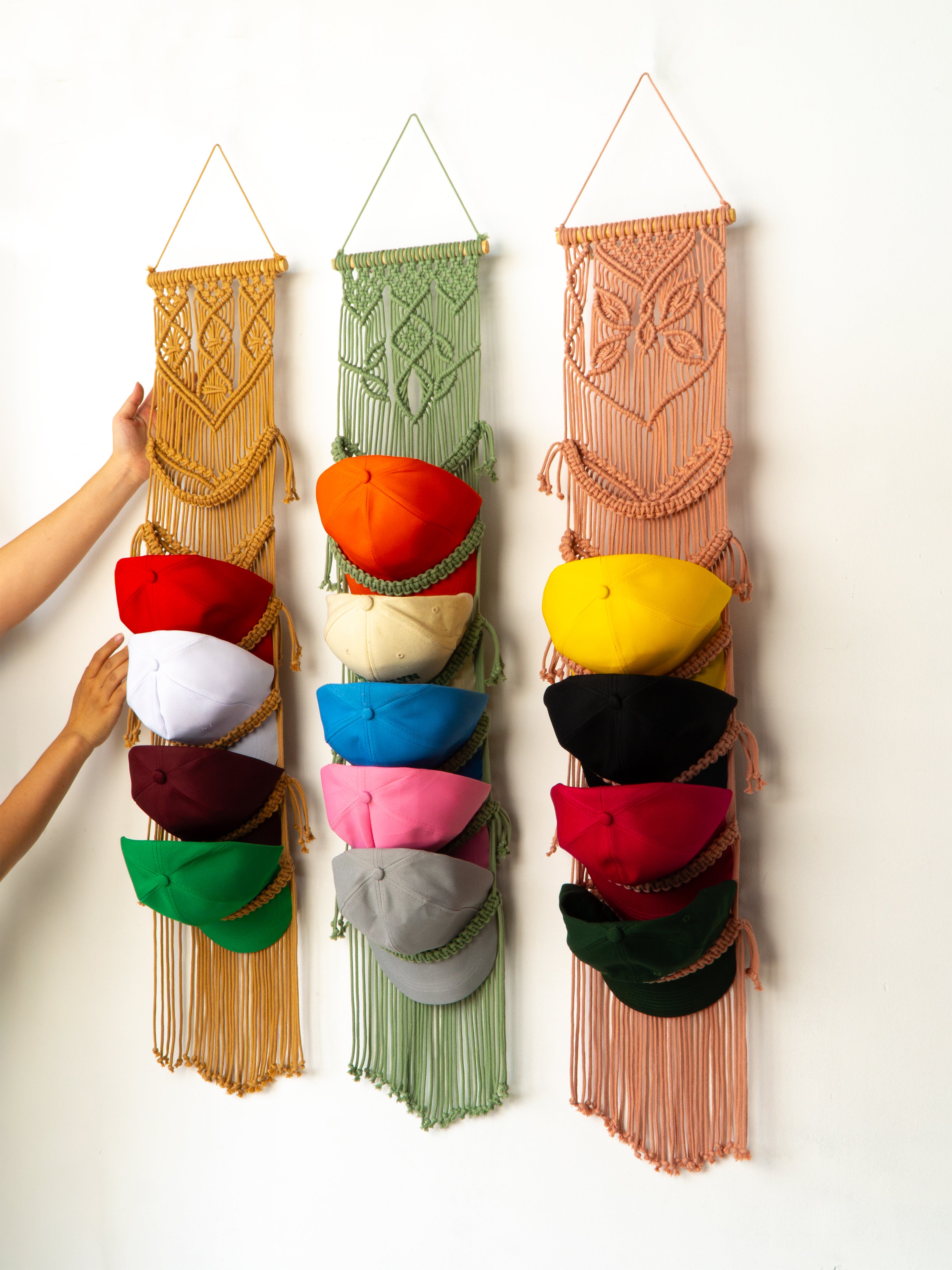 Colorful macrame hat organizer with various colored hats on a white background