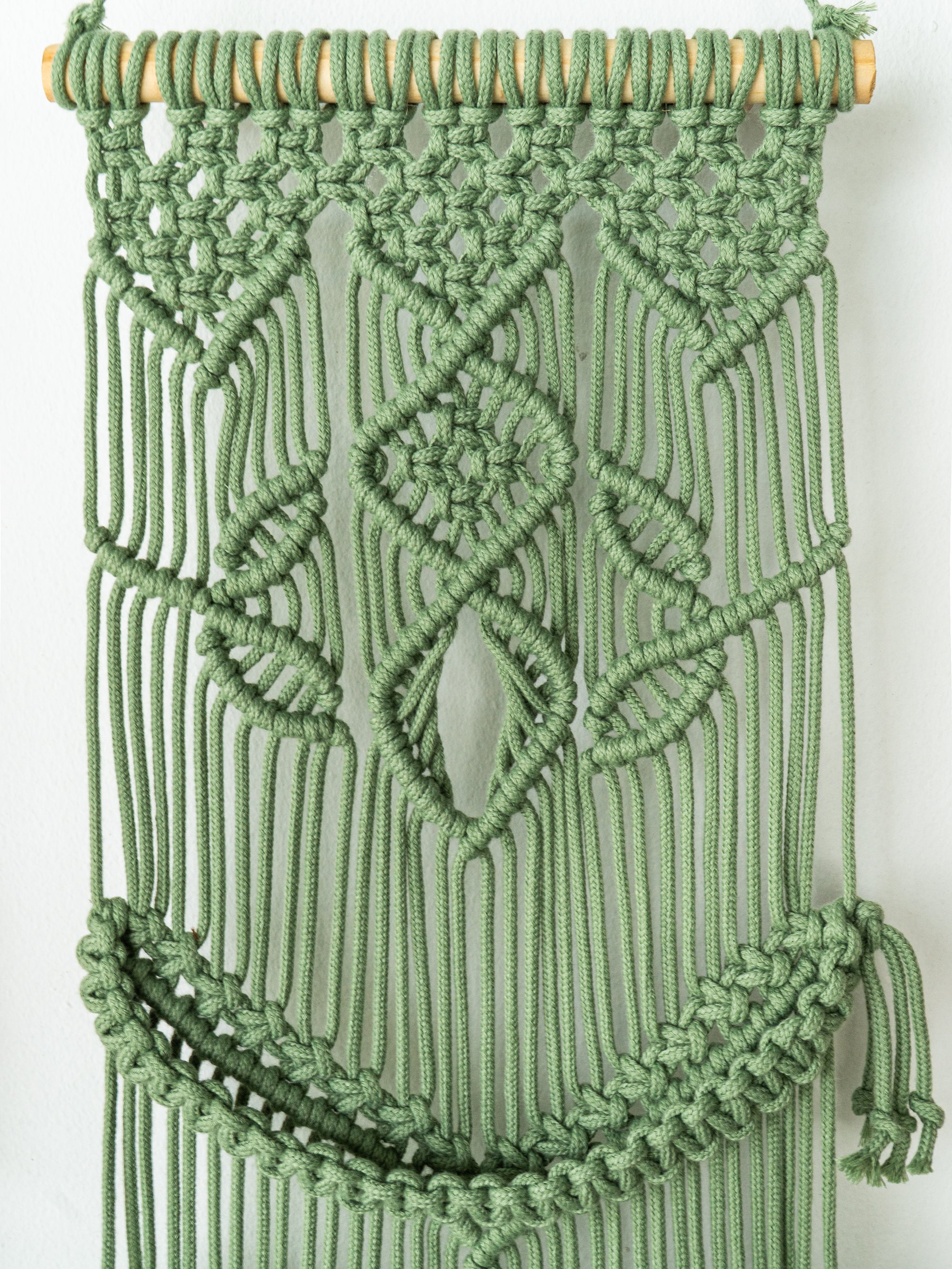 Green macrame wall hanging with intricate patterns on a white background