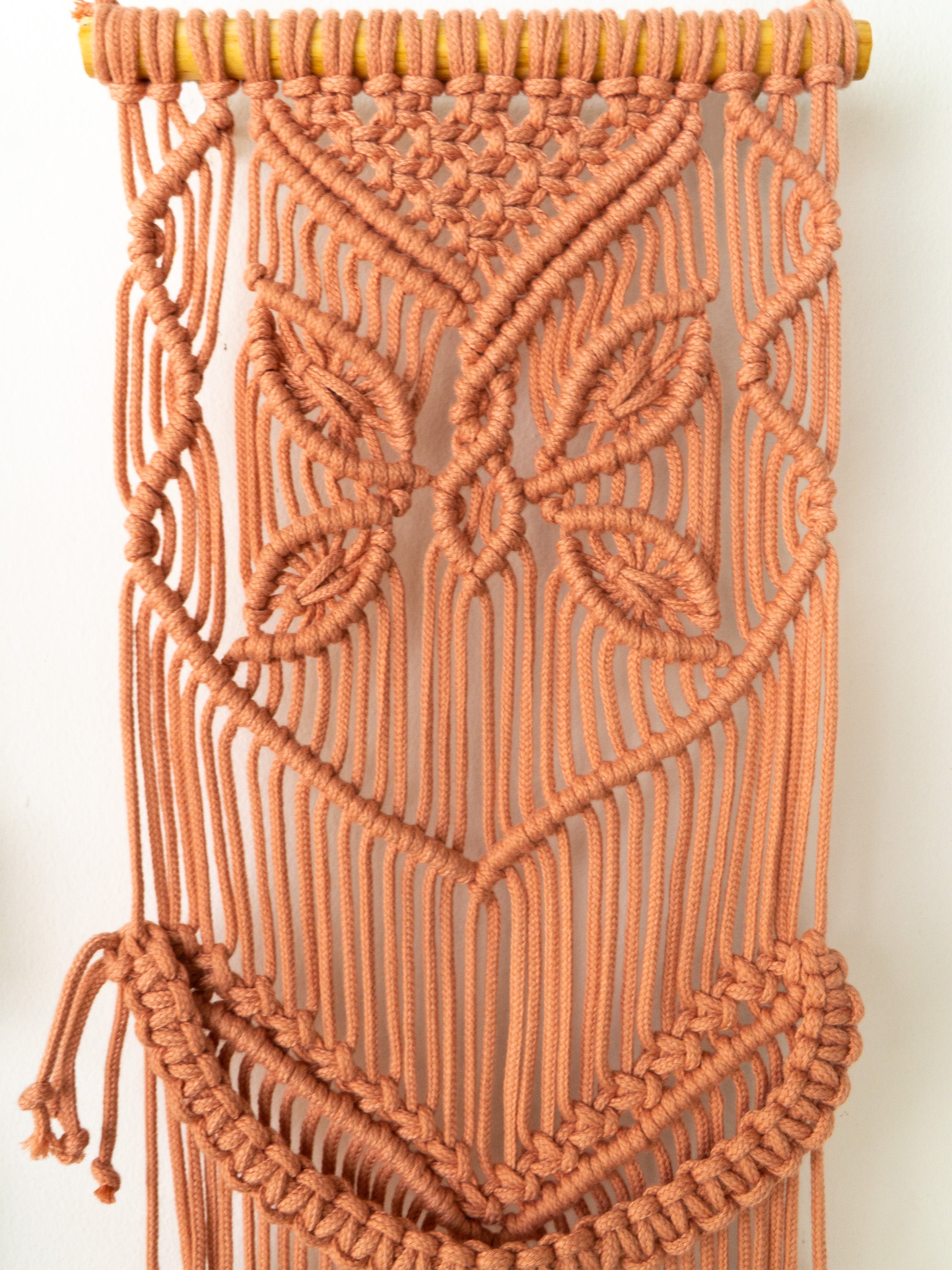Macrame wall hanging with intricate patterns on a plain background