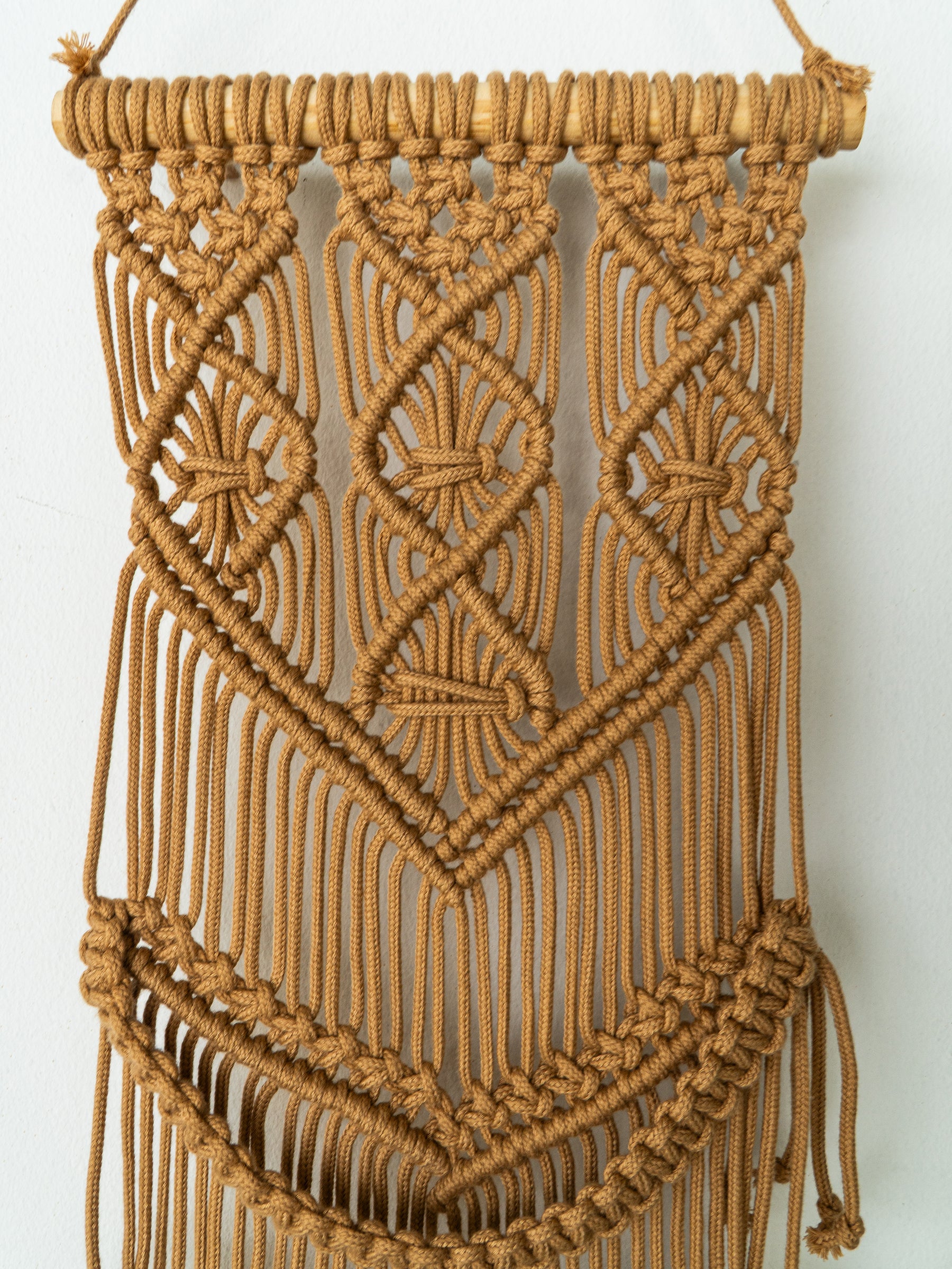 Brown macrame wall hanging with intricate patterns on a white background