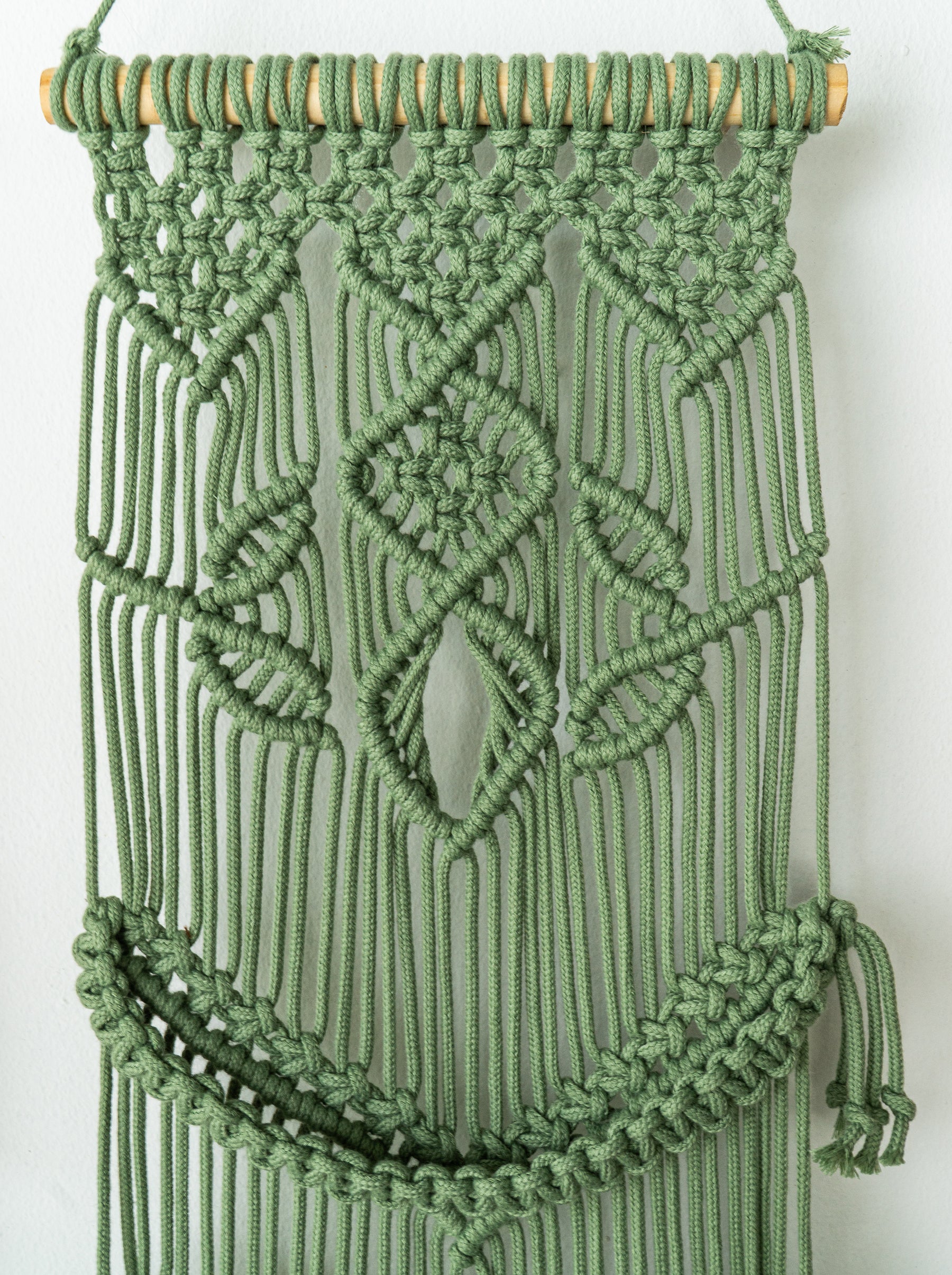 Green macrame wall hanging with geometric pattern on a white background