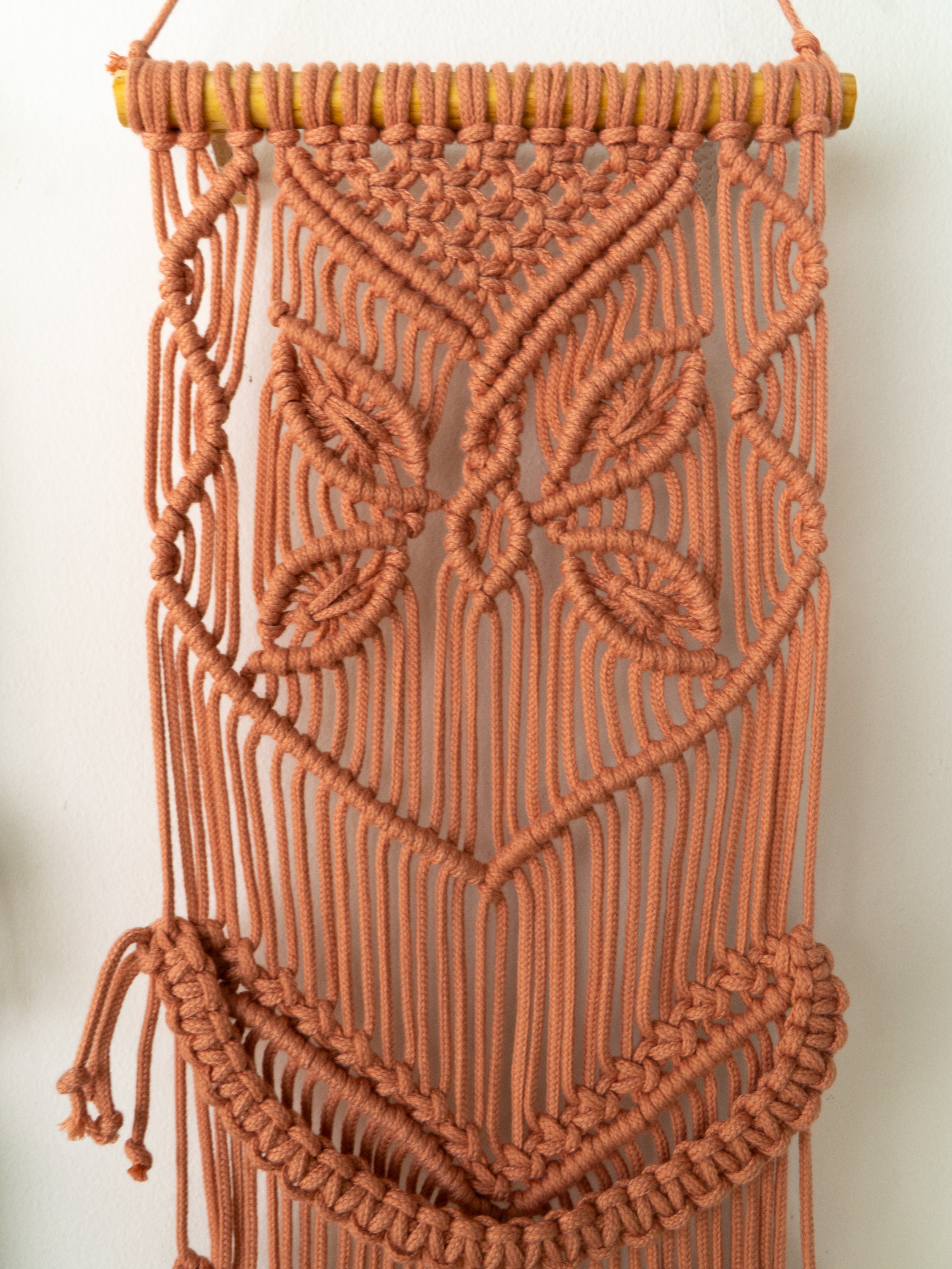 Brown macrame wall hanging with intricate patterns on a white background