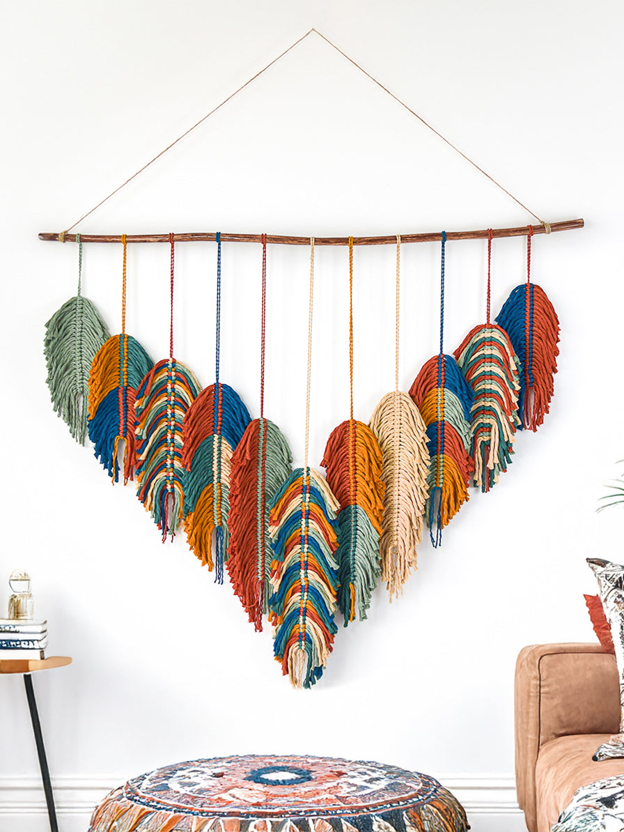 Colorful feather wall hanging in a room with a couch and side table.