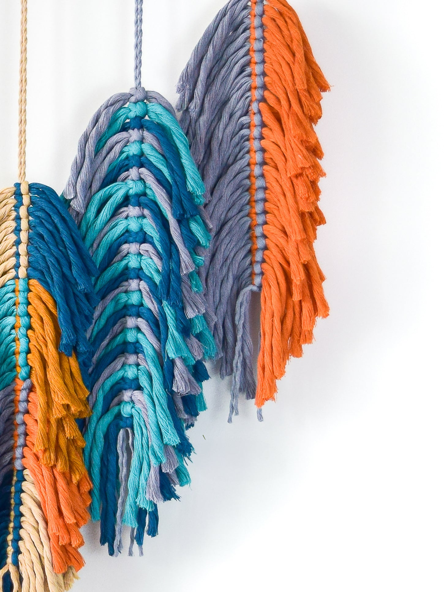 Colorful yarn wall hanging with blue, orange, and gray fringes on a white background