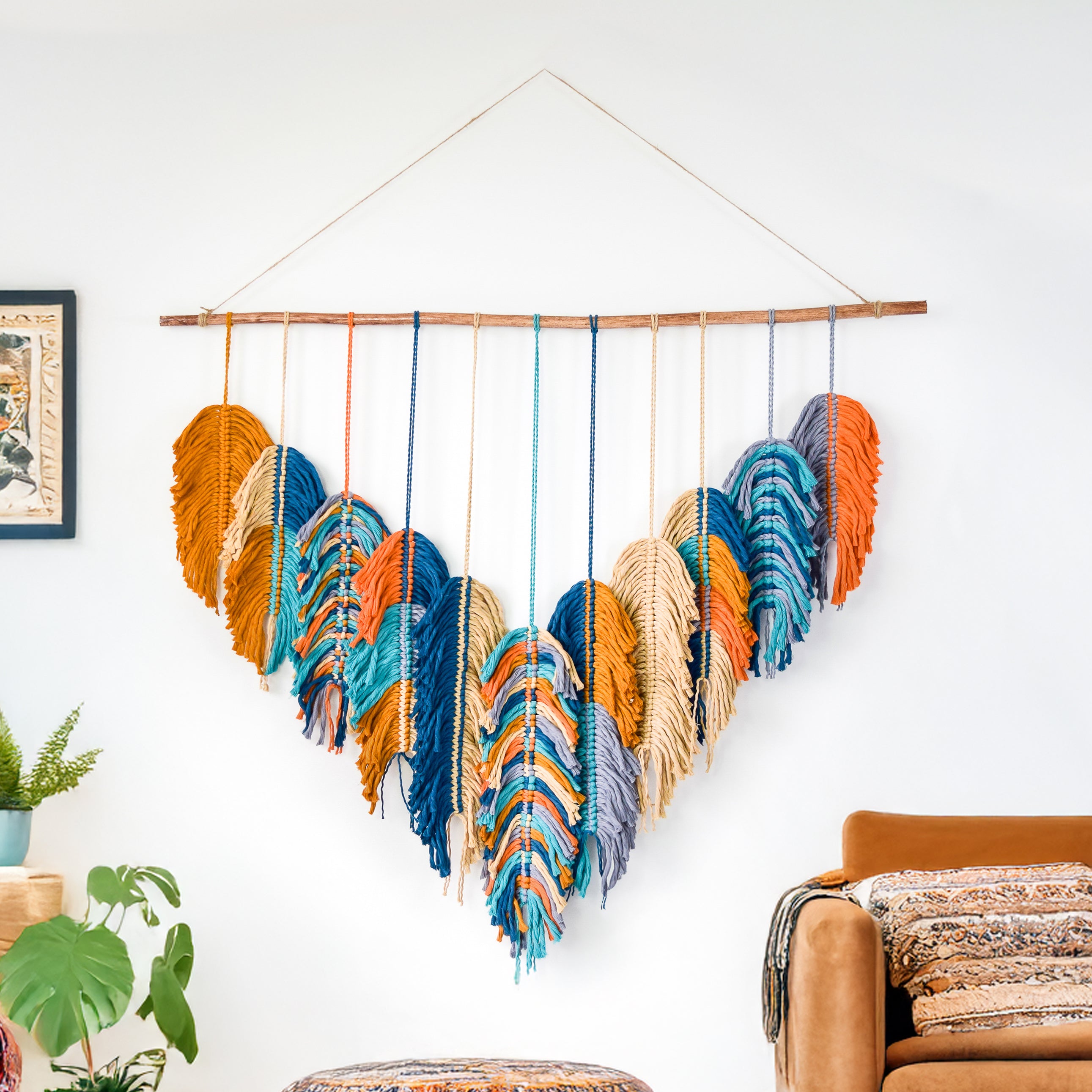 Colorful woven wall hanging on a white wall with a couch and plants in the background