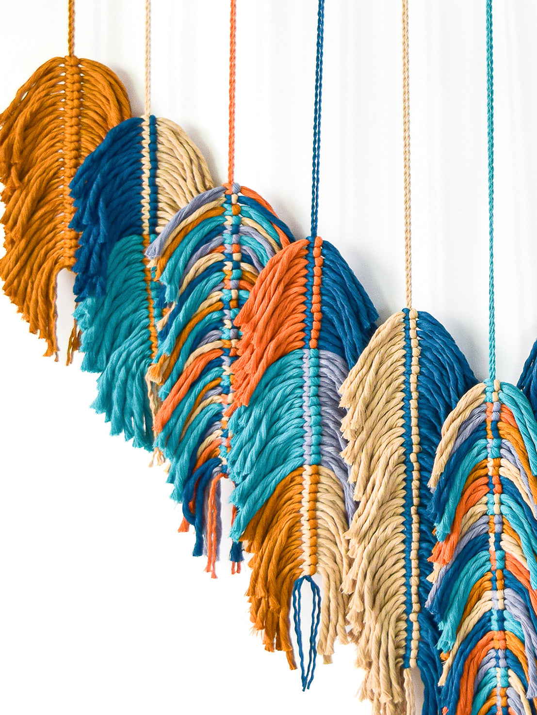 Colorful macrame wall hanging with wavy patterns on a white background