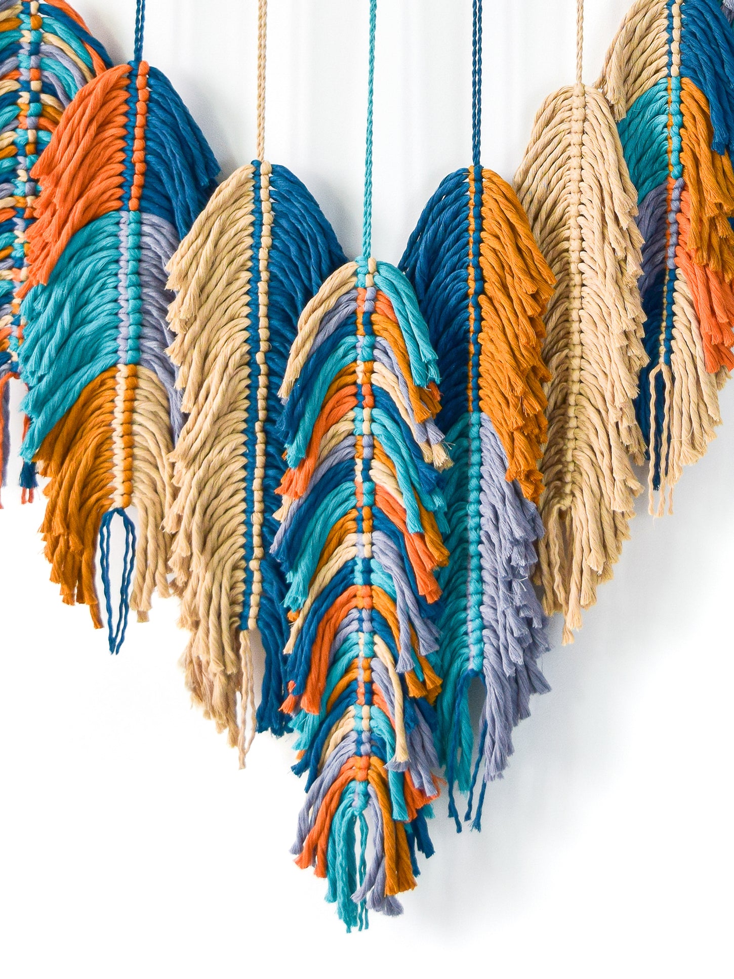 Colorful macrame wall hanging with blue, orange, and beige threads on a white background