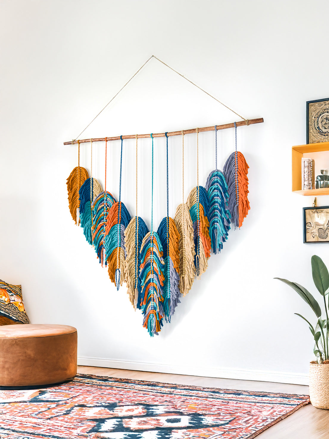 Colorful wall hanging with feathers in a room with a couch and plant.