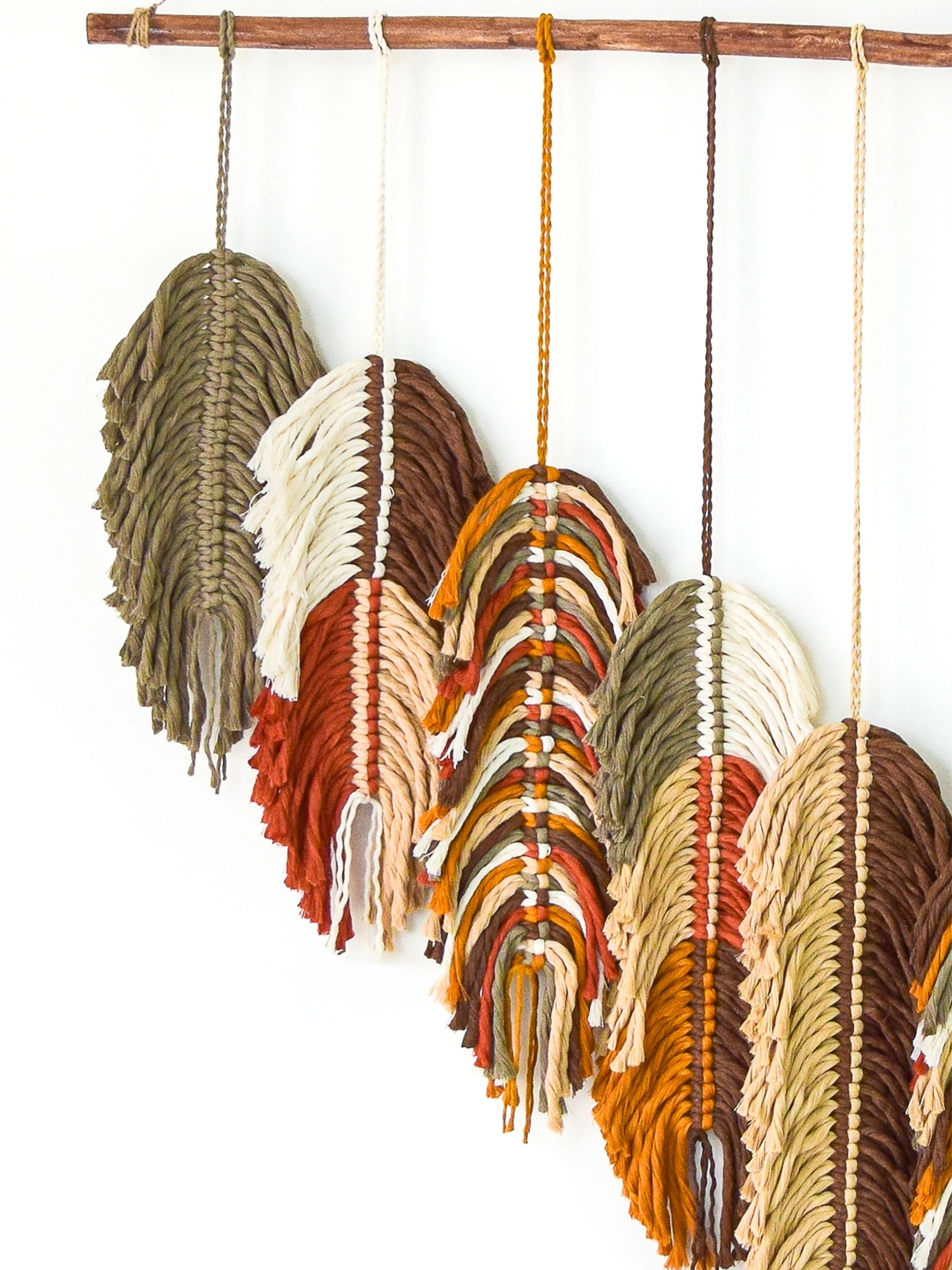 Set of macrame wall hangings in earthy tones hanging on a wooden rod.