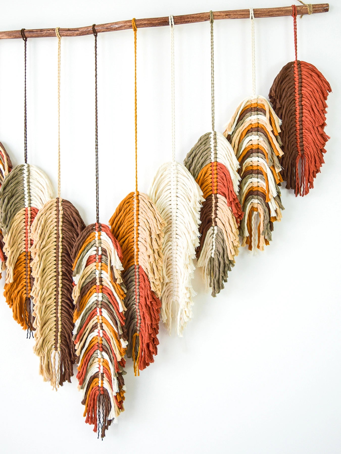 Decorative macrame wall hanging with feather shapes in autumn colors on a white background