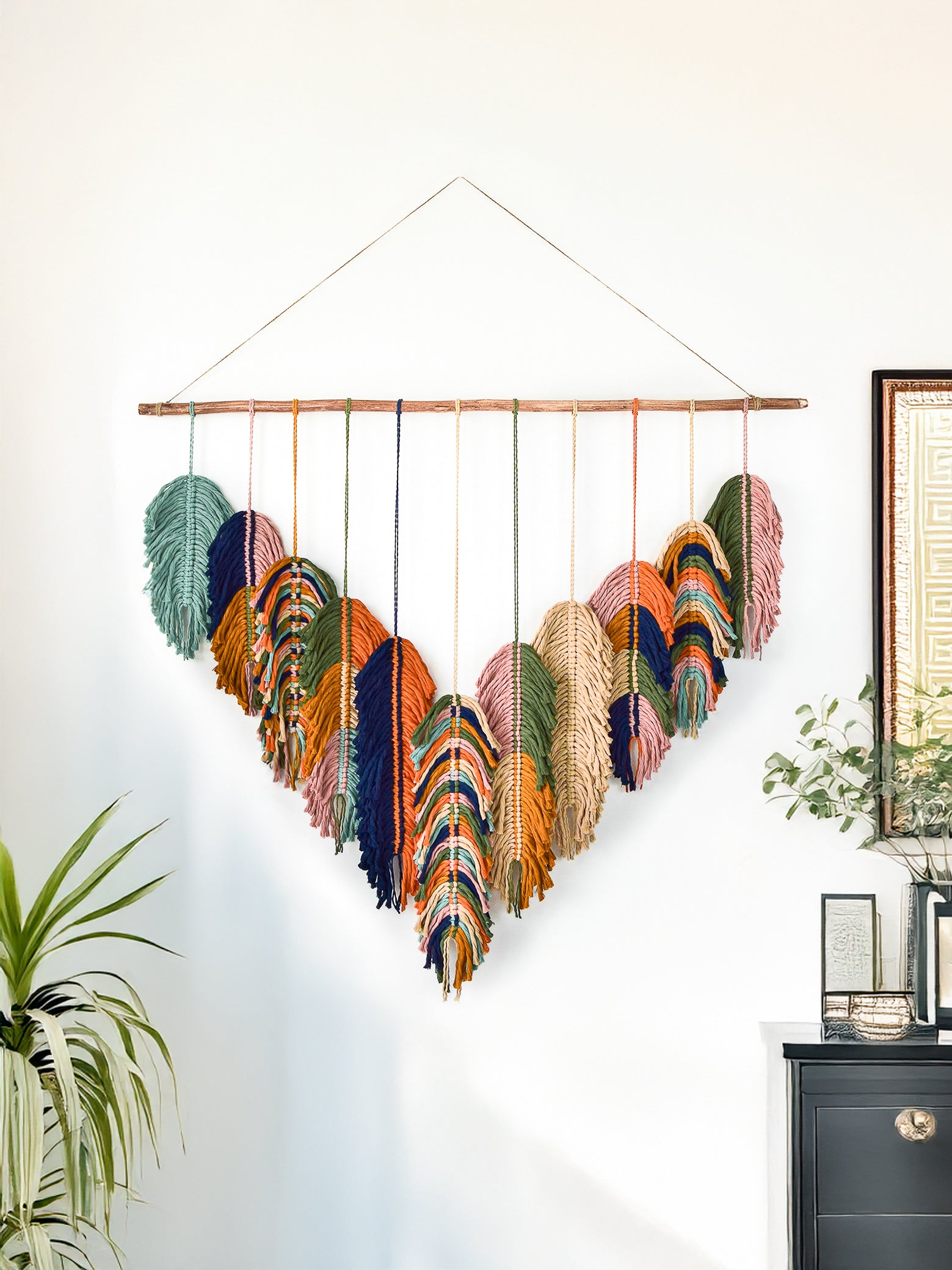Decorative wall hanging with colorful feathers on a white wall.