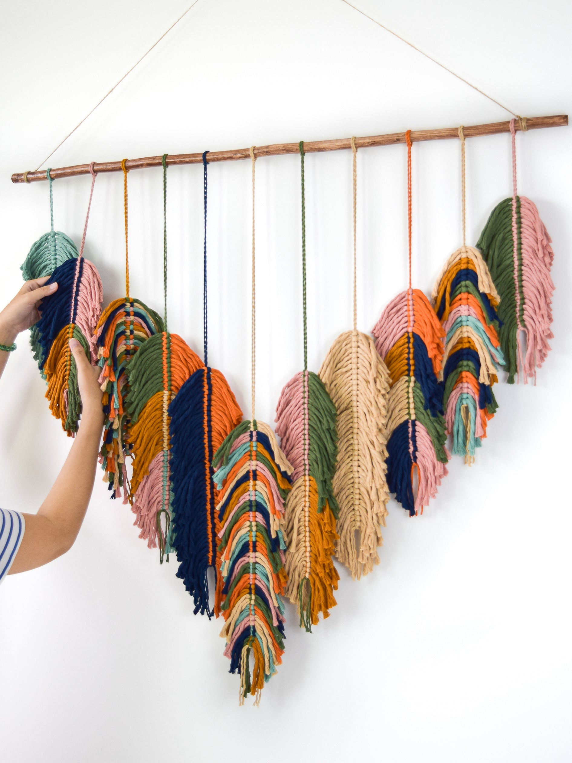 Colorful yarn bundles hanging from a wooden rod against a white wall.