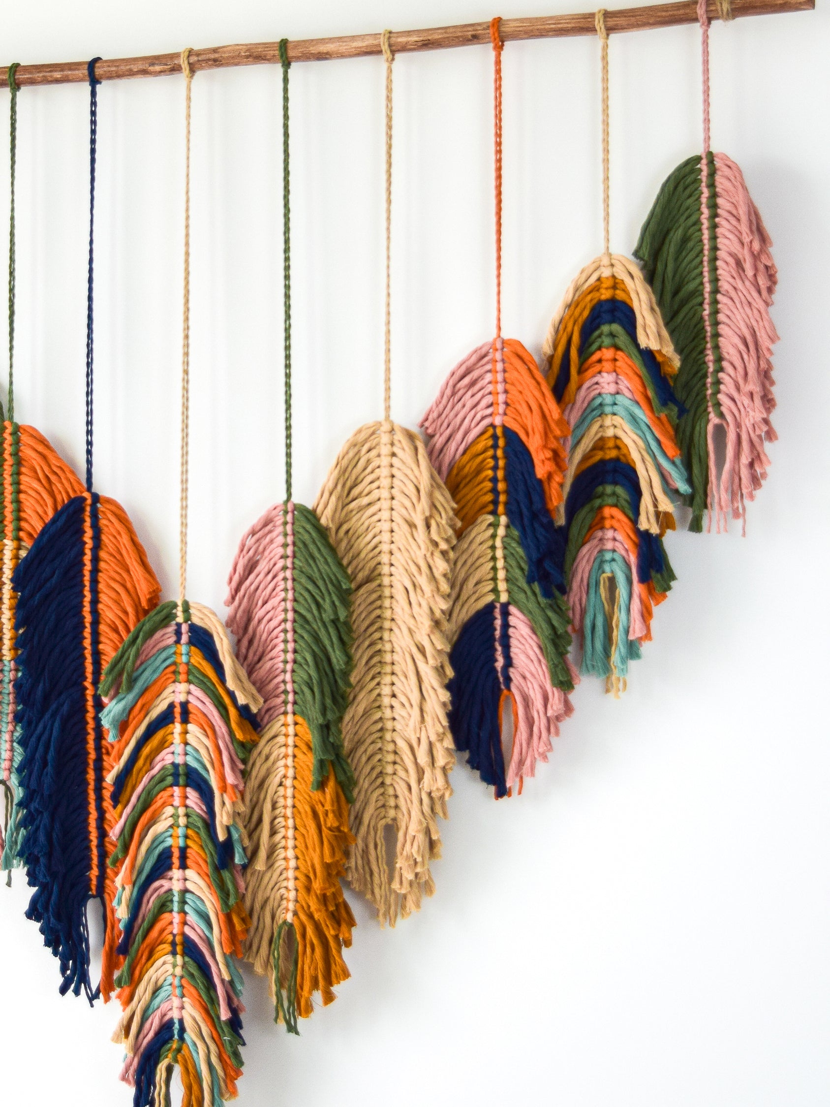 Colorful macrame wall hanging with feather shapes on a white background