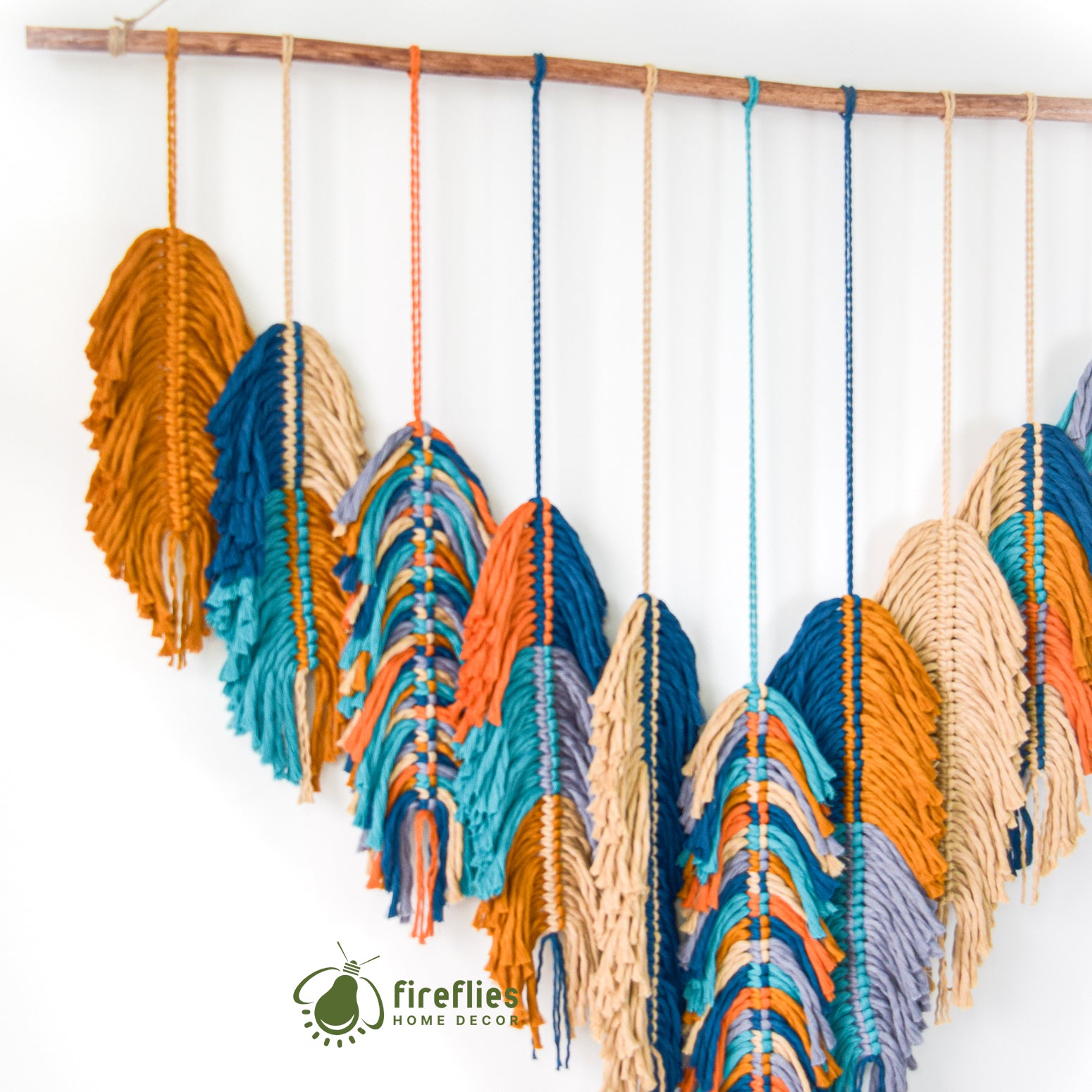 Colorful yarn feather decorations hanging on a wooden rod against a white background, with 'Fireflies Home Decor' branding.