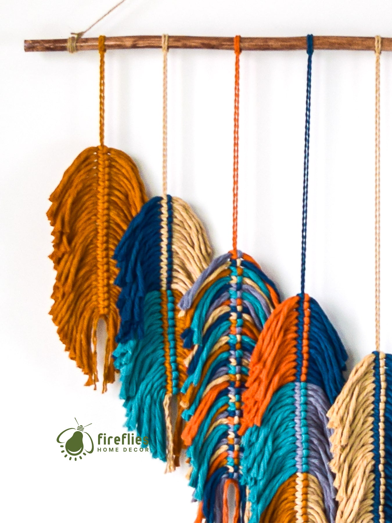 Colorful woven wall art with a wooden stick on a white background, featuring the brand 'Fireflies Home Decor'.