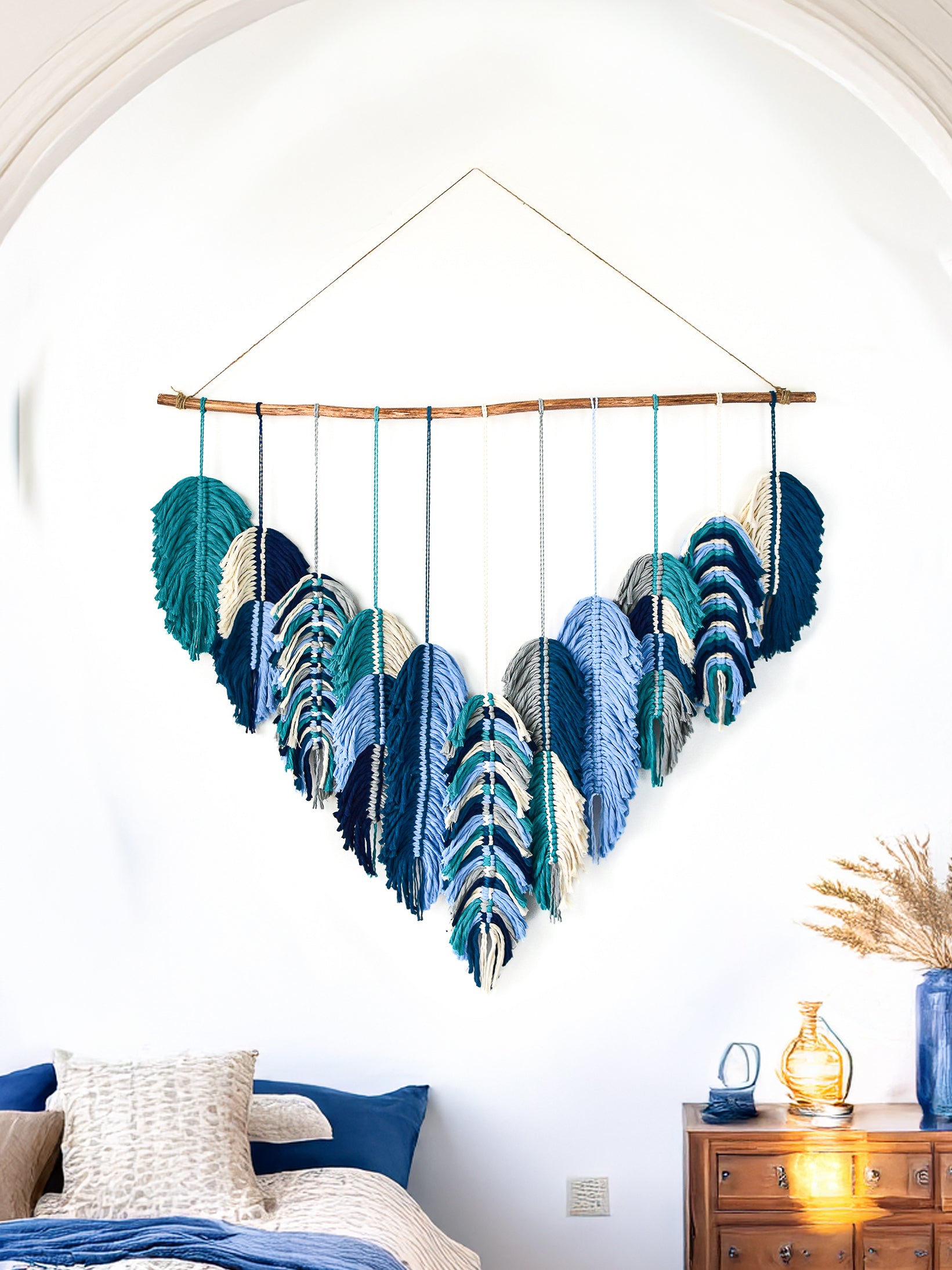 Colorful wall hanging with leaf-like designs in a room with a plant and small table.