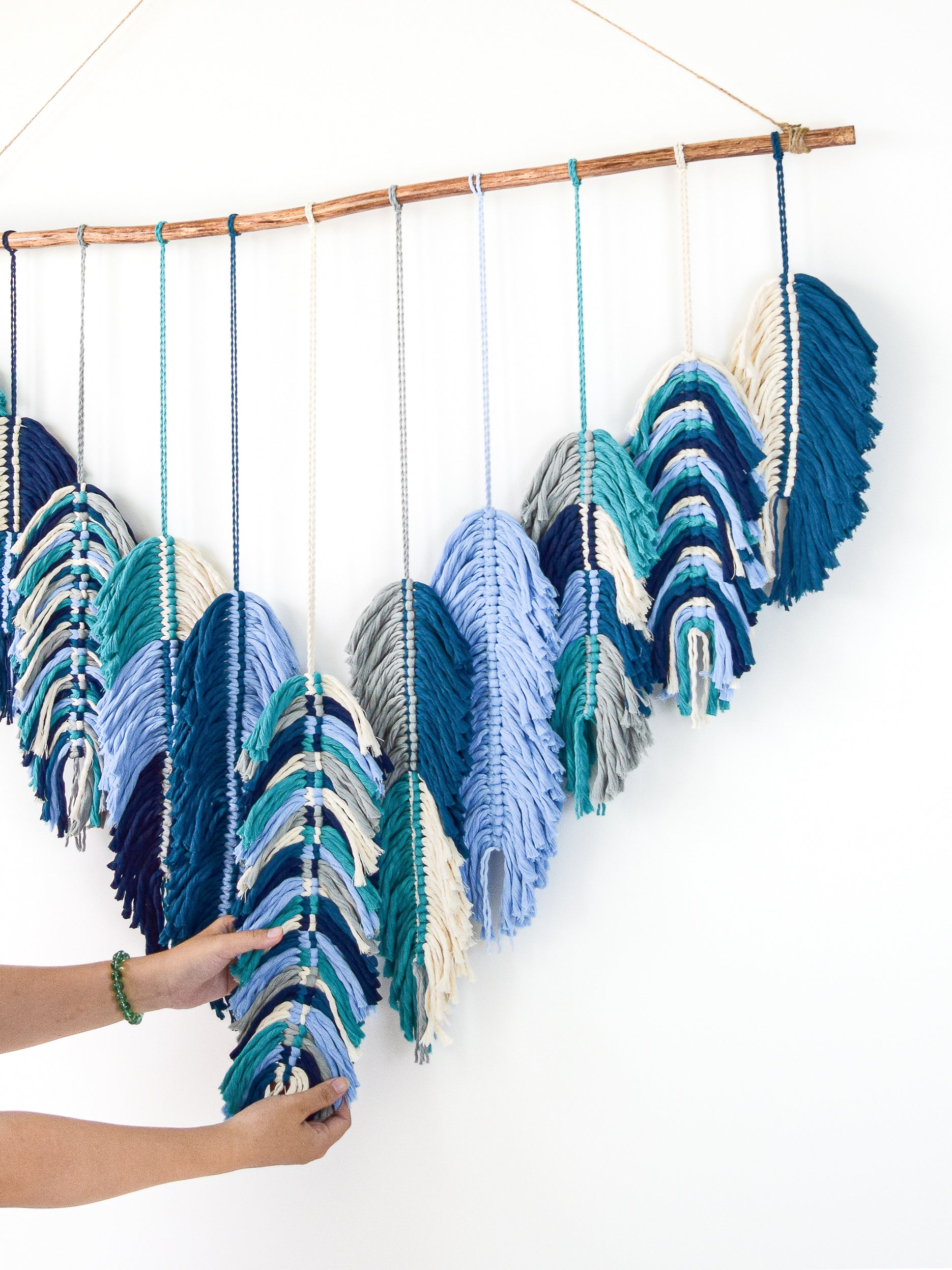 Woven wall art with blue and green patterns on a white background