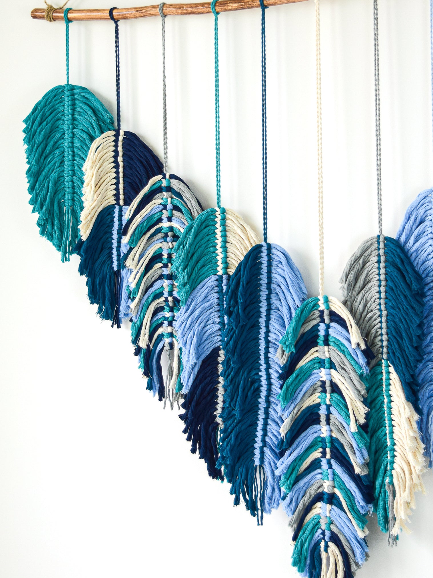 Colorful yarn feather decorations hanging on a wooden rod against a white background