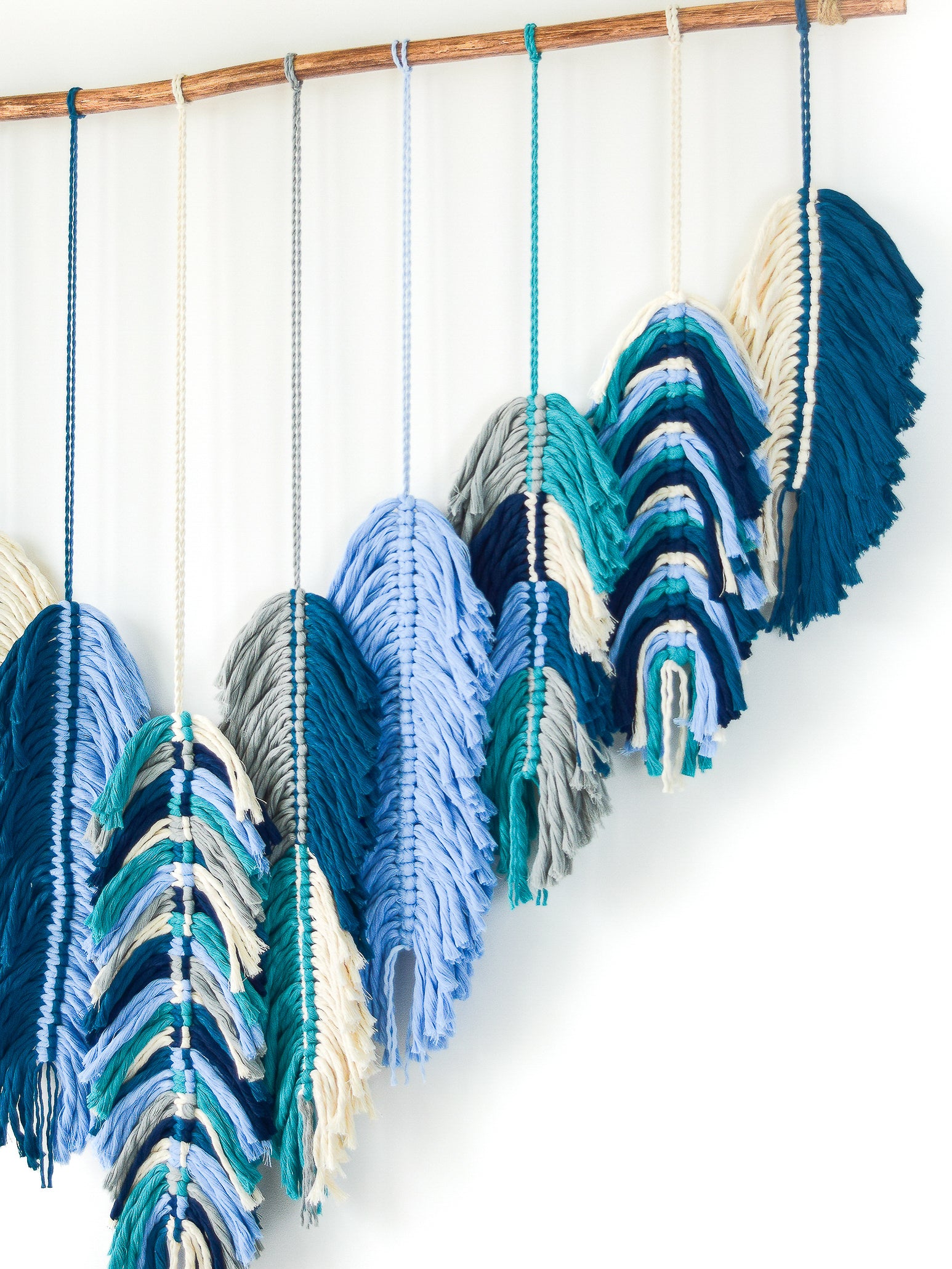 Colorful yarn skeins hanging on a wooden rod against a white background