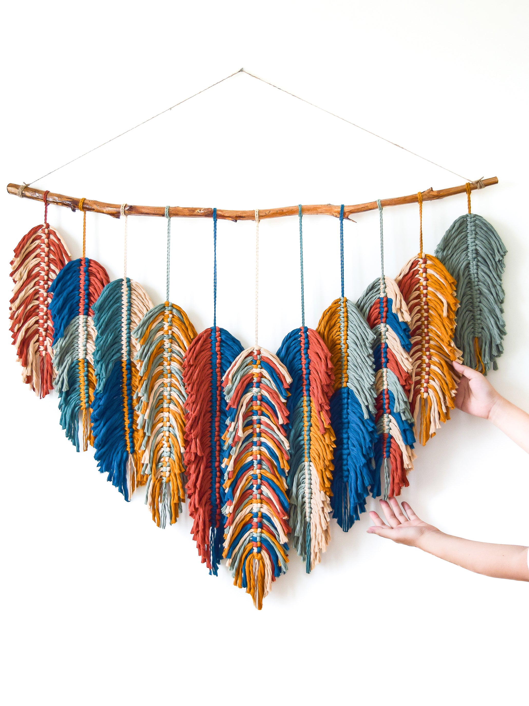 Colorful feather-like decorations hanging from a branch against a white background