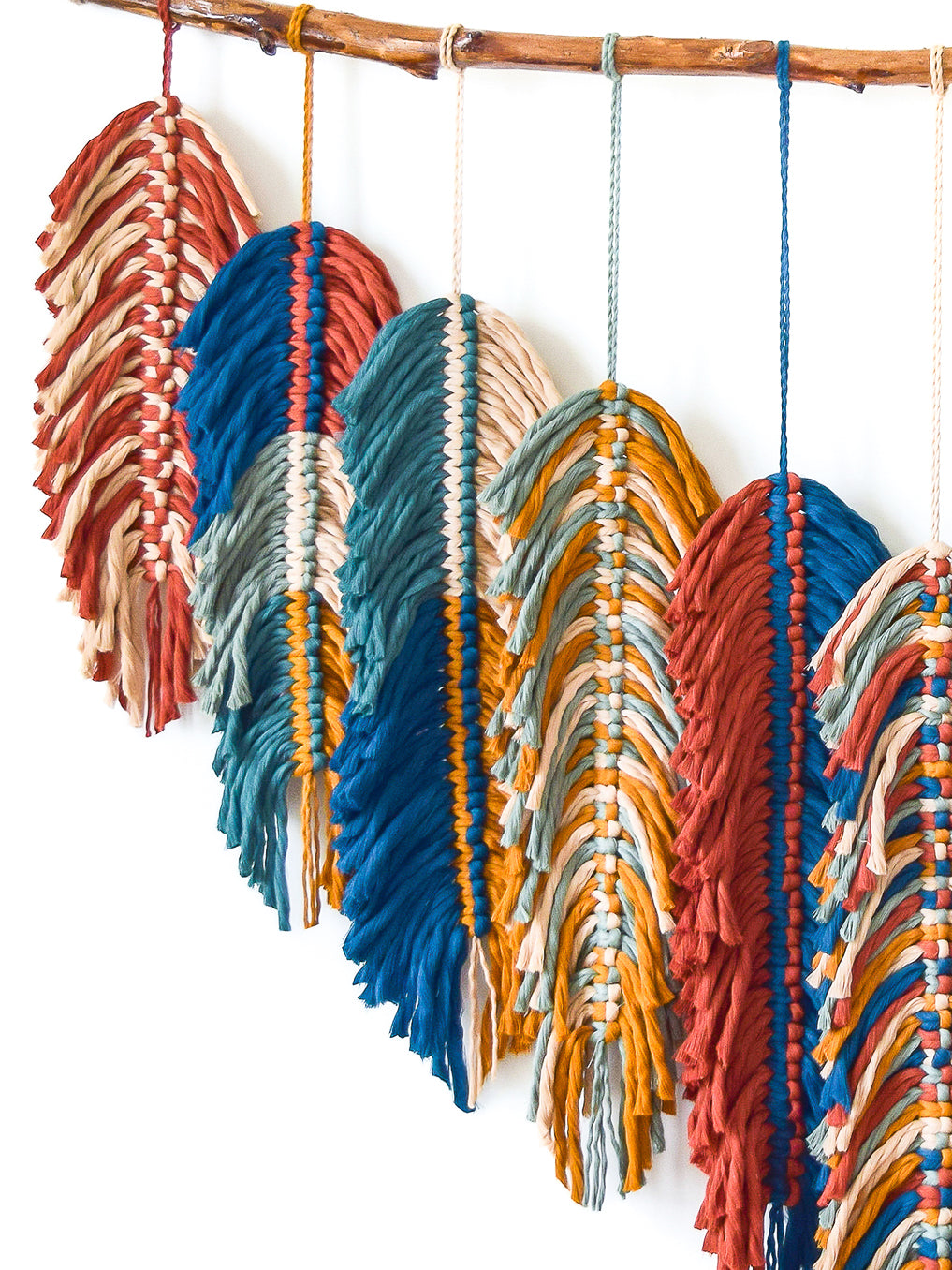 Colorful feather-shaped decorations hanging from a bamboo rod against a white background