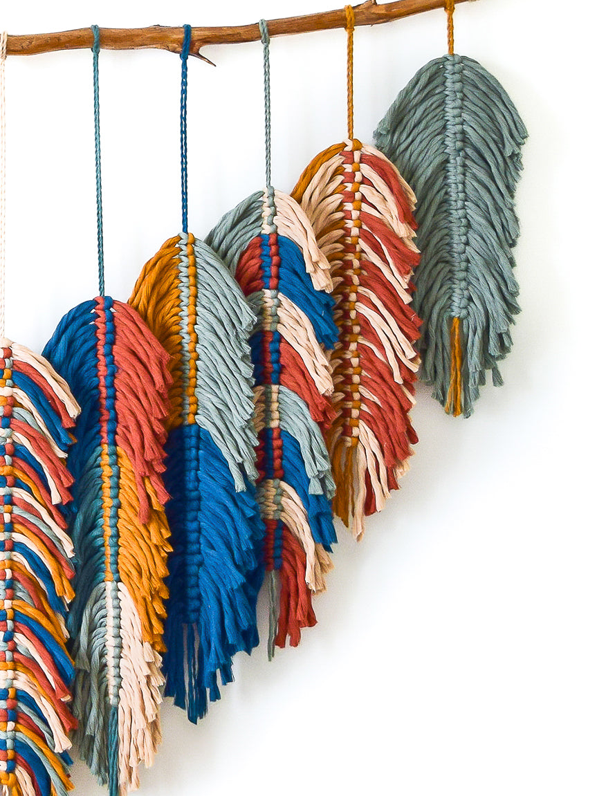 Colorful macramé wall hanging with a branch on a white background