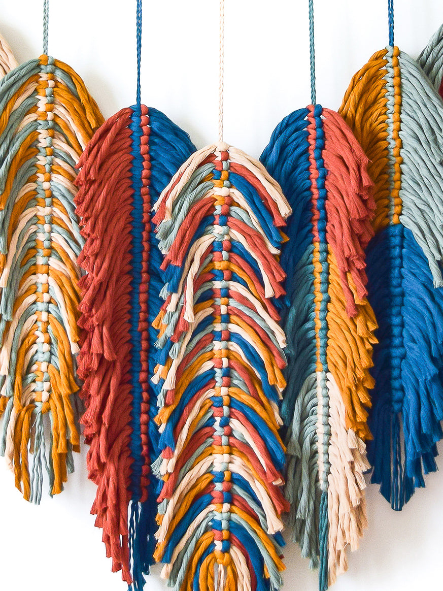 Colorful yarn feather decorations hanging against a white background