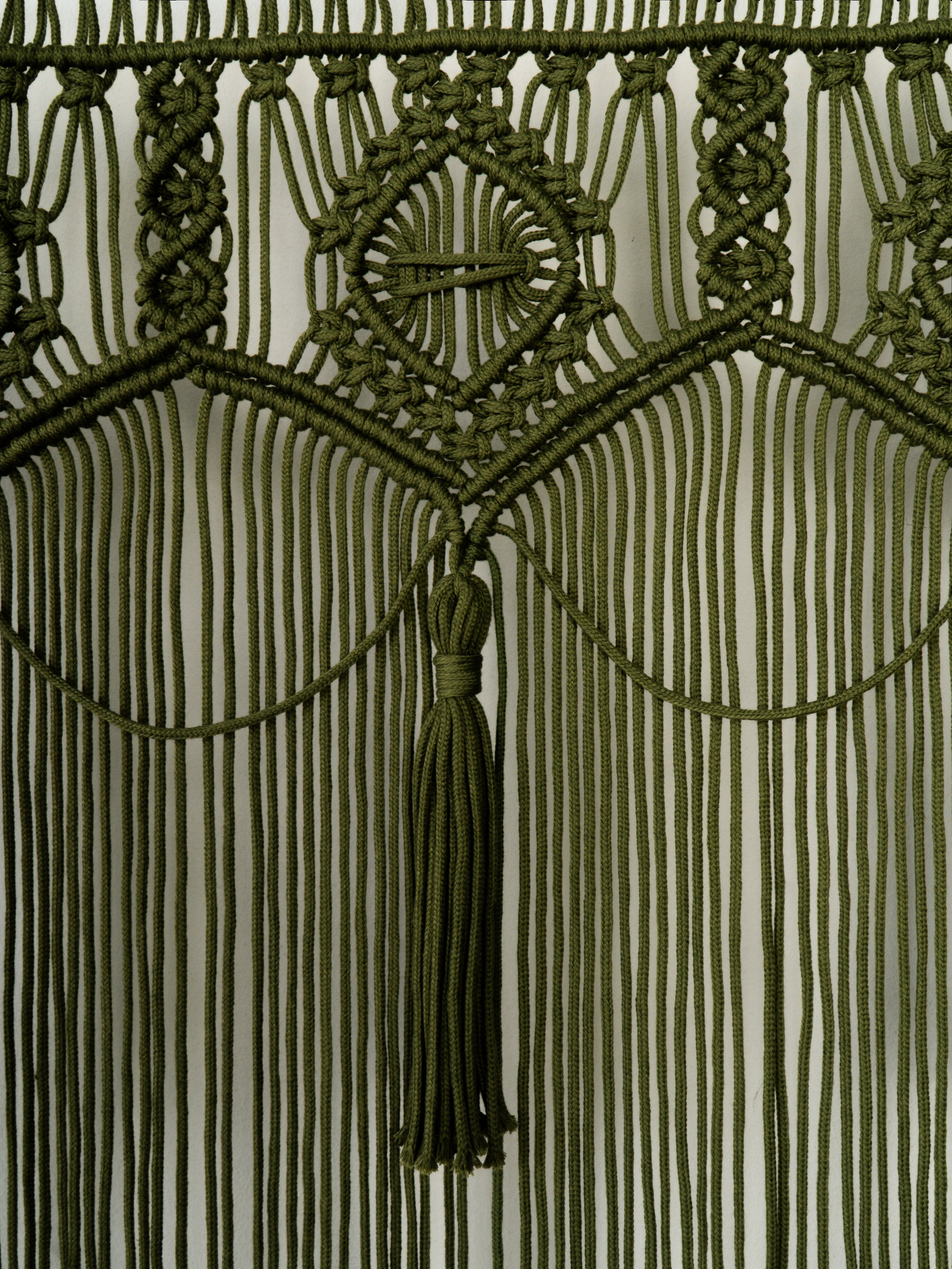Close-up of a green macrame wall hanging with geometric patterns and a tassel.