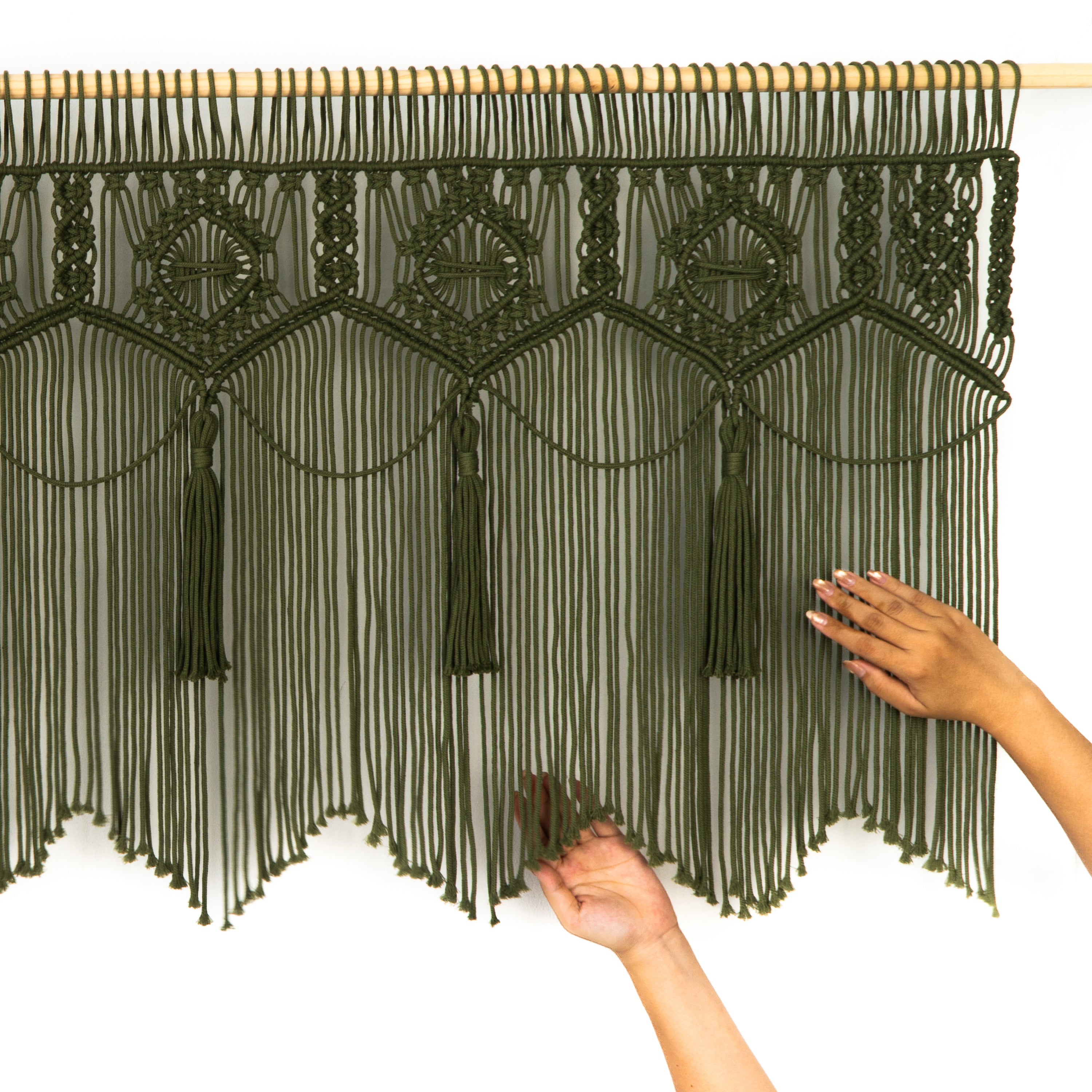 Black macrame curtain with tassels held by hands against a white background