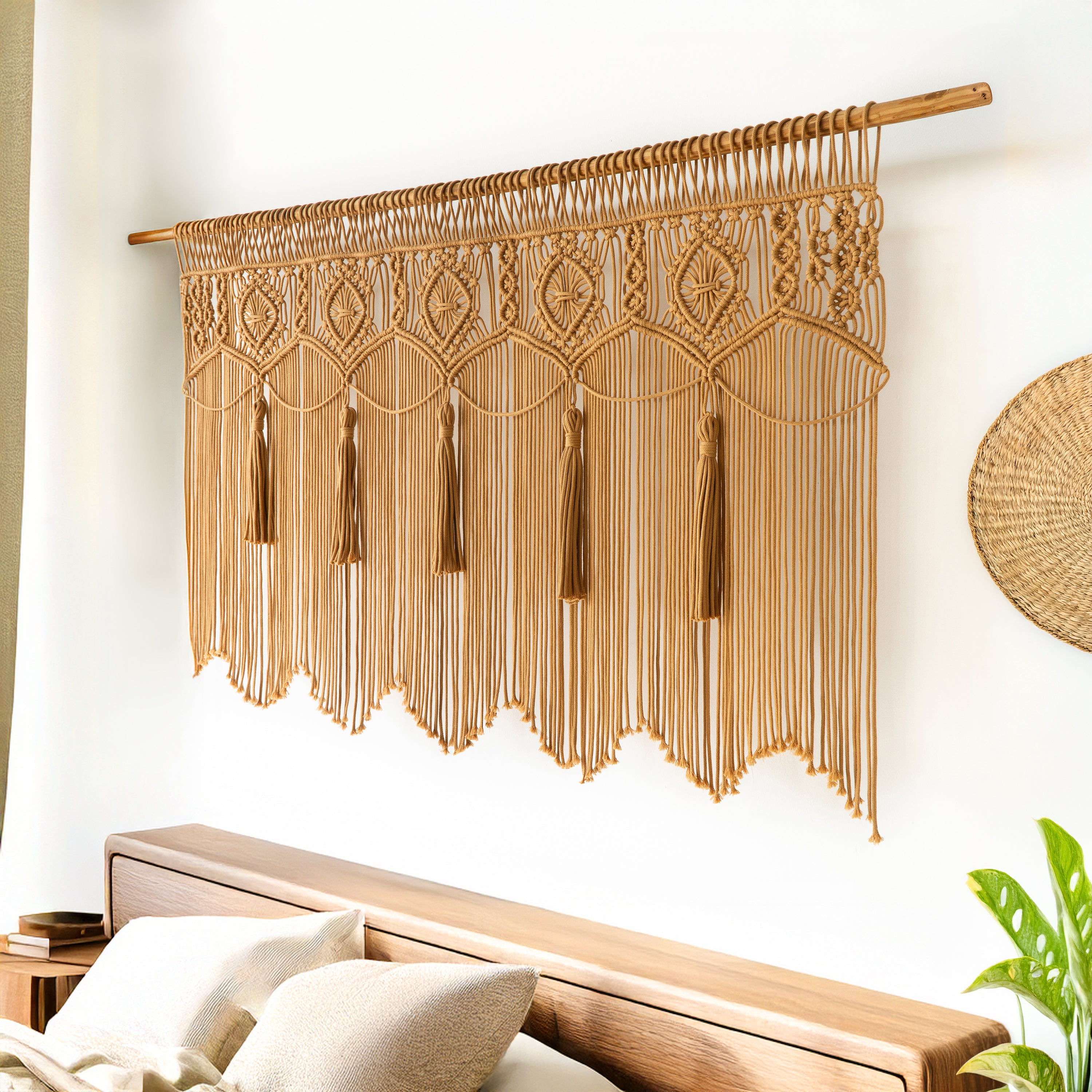 Macrame wall hanging with tassels on a white wall above a wooden headboard.