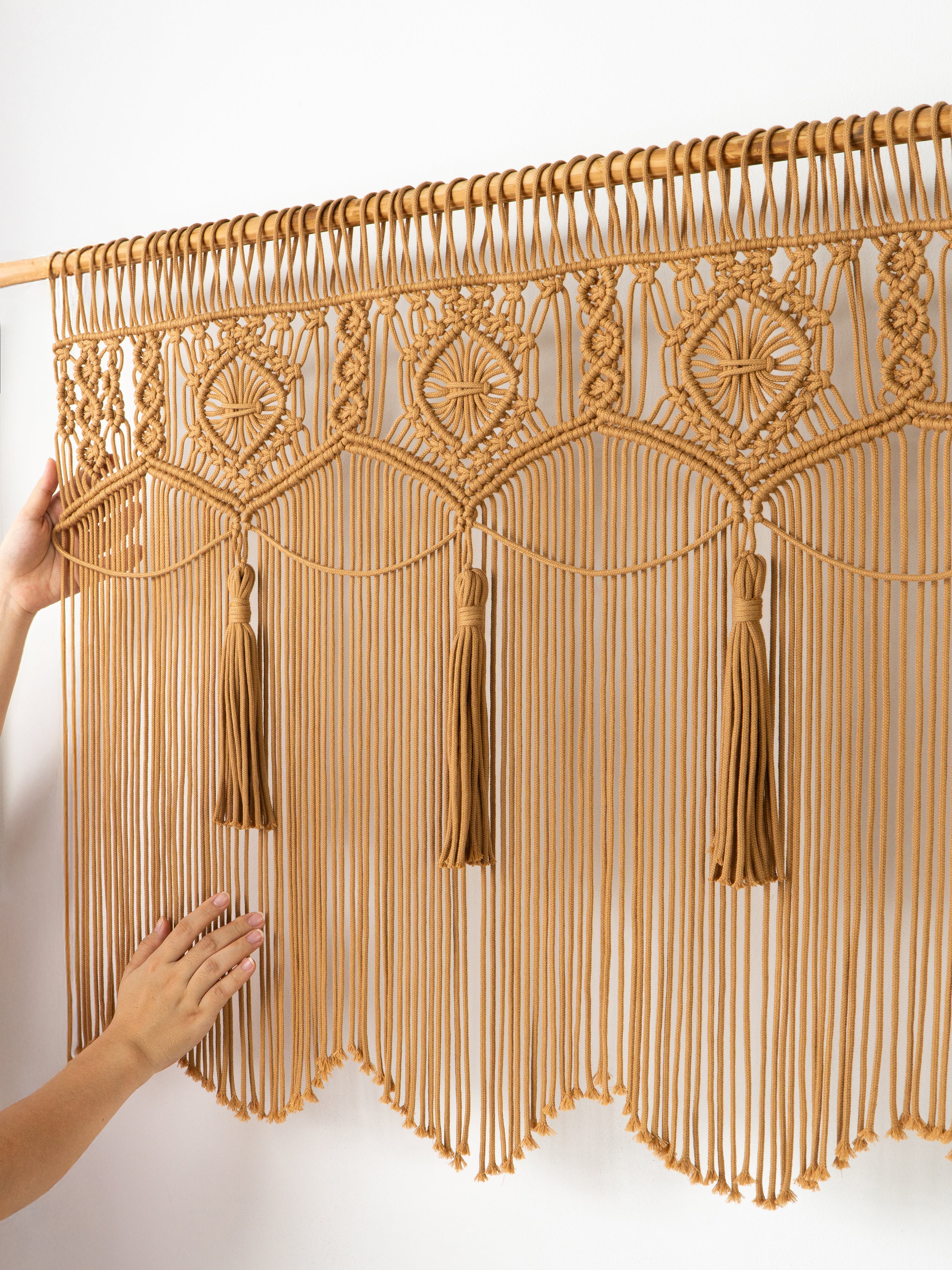 Decorative macrame curtain with tassels held by a hand against a white background