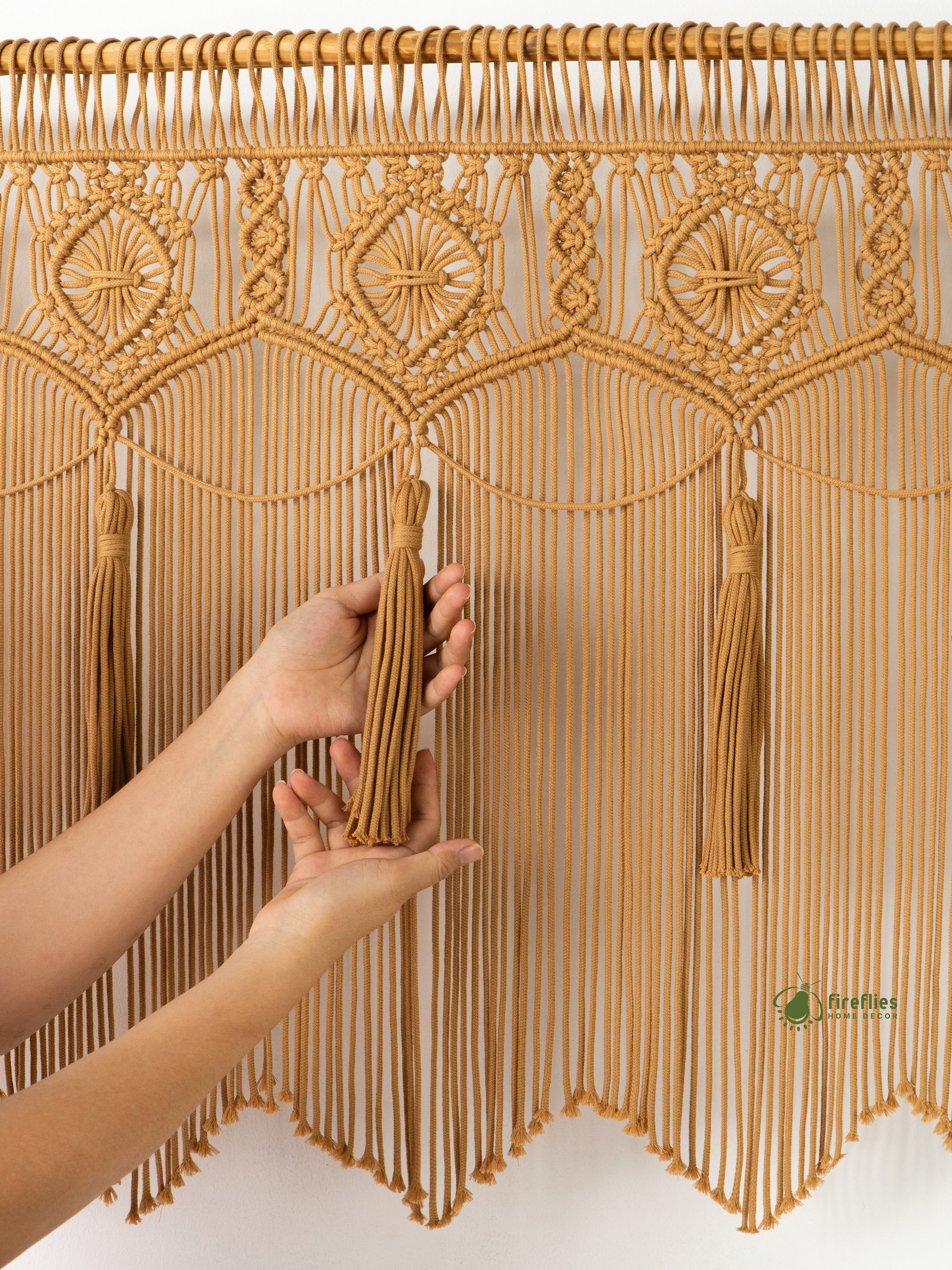 Hand holding a tassel in front of a decorative macrame curtain with intricate patterns.
