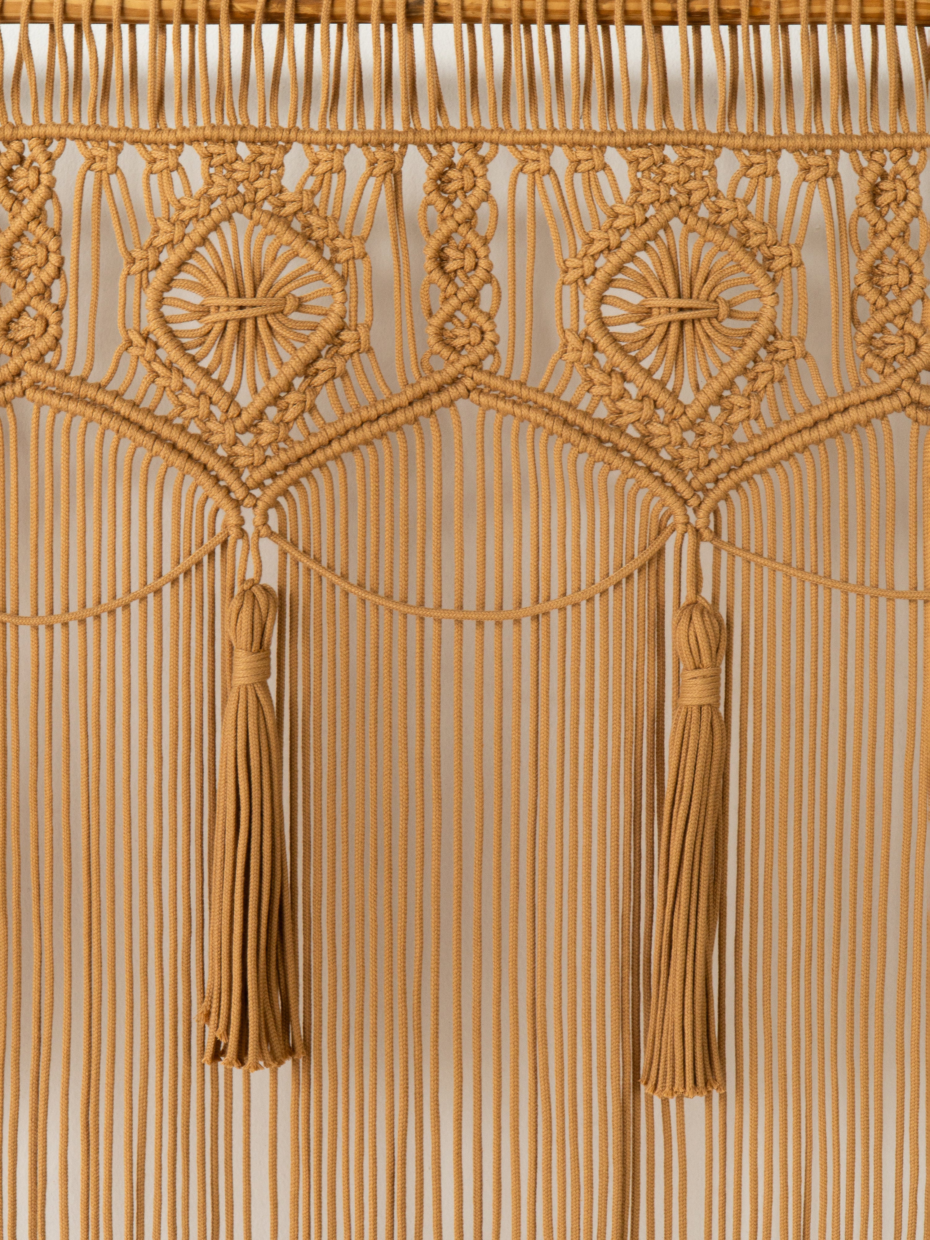 Close-up of a beige macrame wall hanging with tassels on a beige background