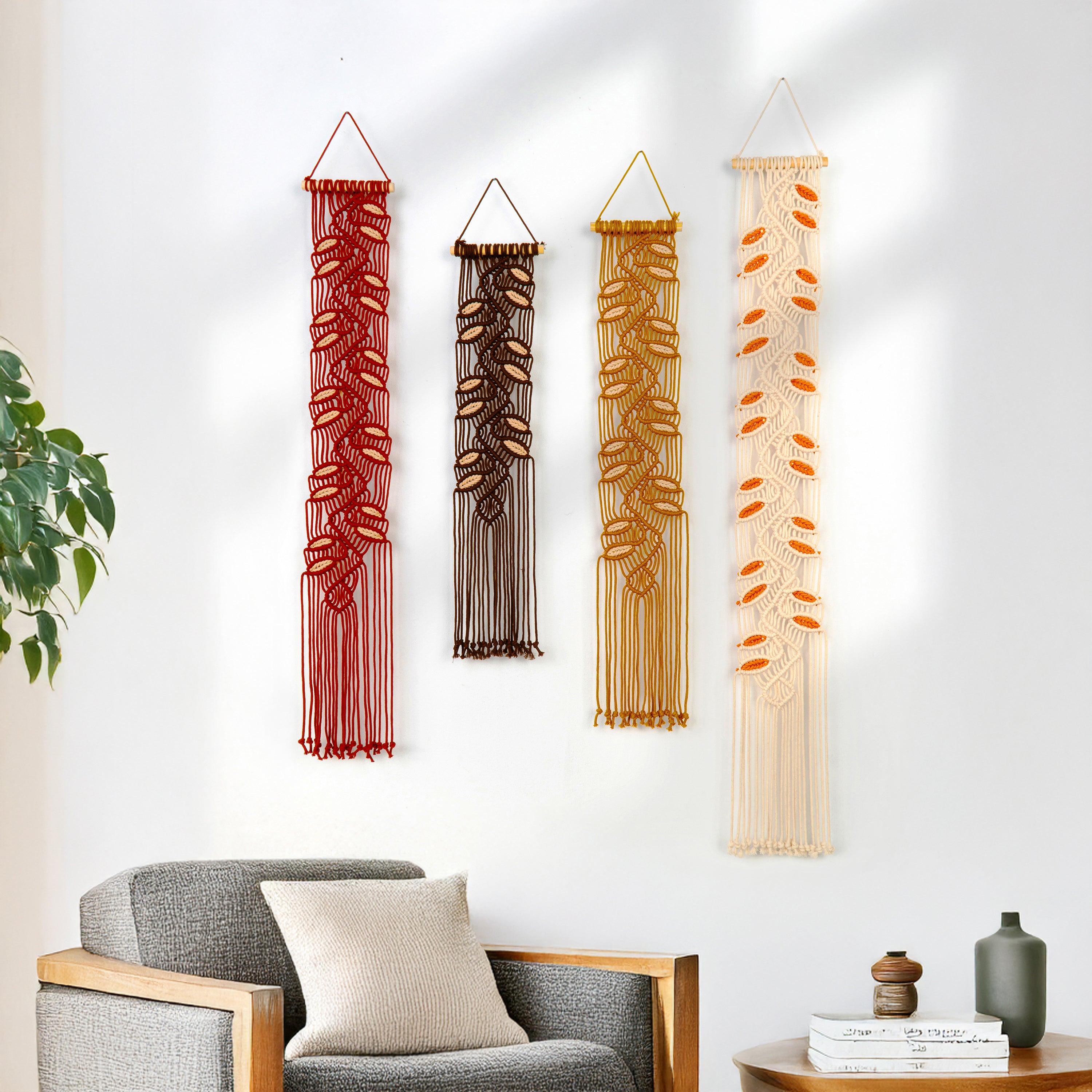 Four macrame wall hangings of different colors hanging on a white wall.