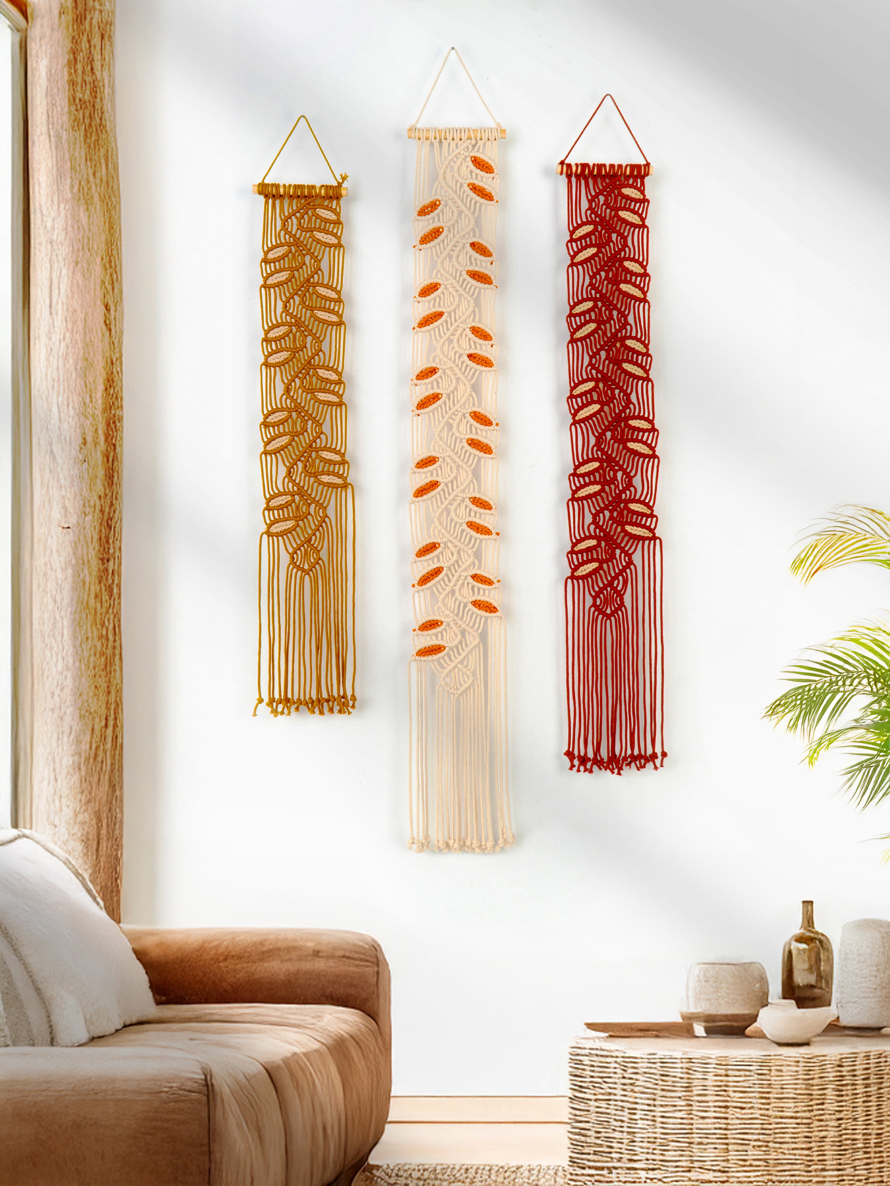Three macrame wall hangings in different designs on a white wall with a living room setting.