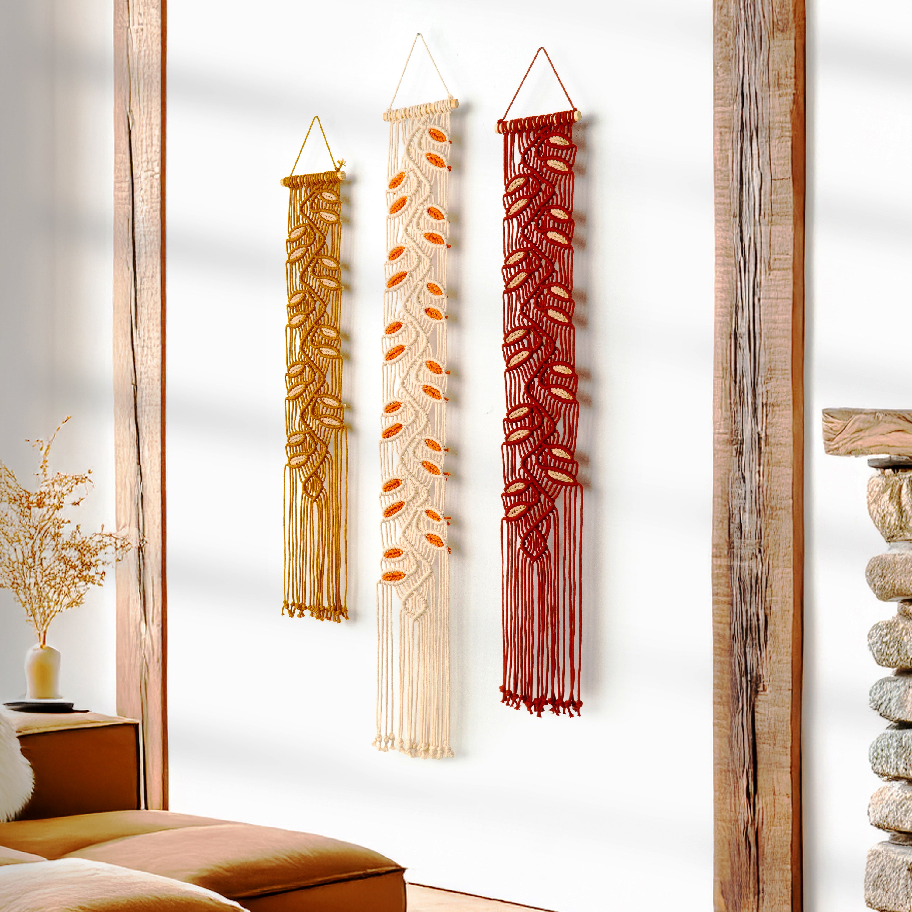 Three decorative wall hangings in gold, beige, and red hanging on a white wall.
