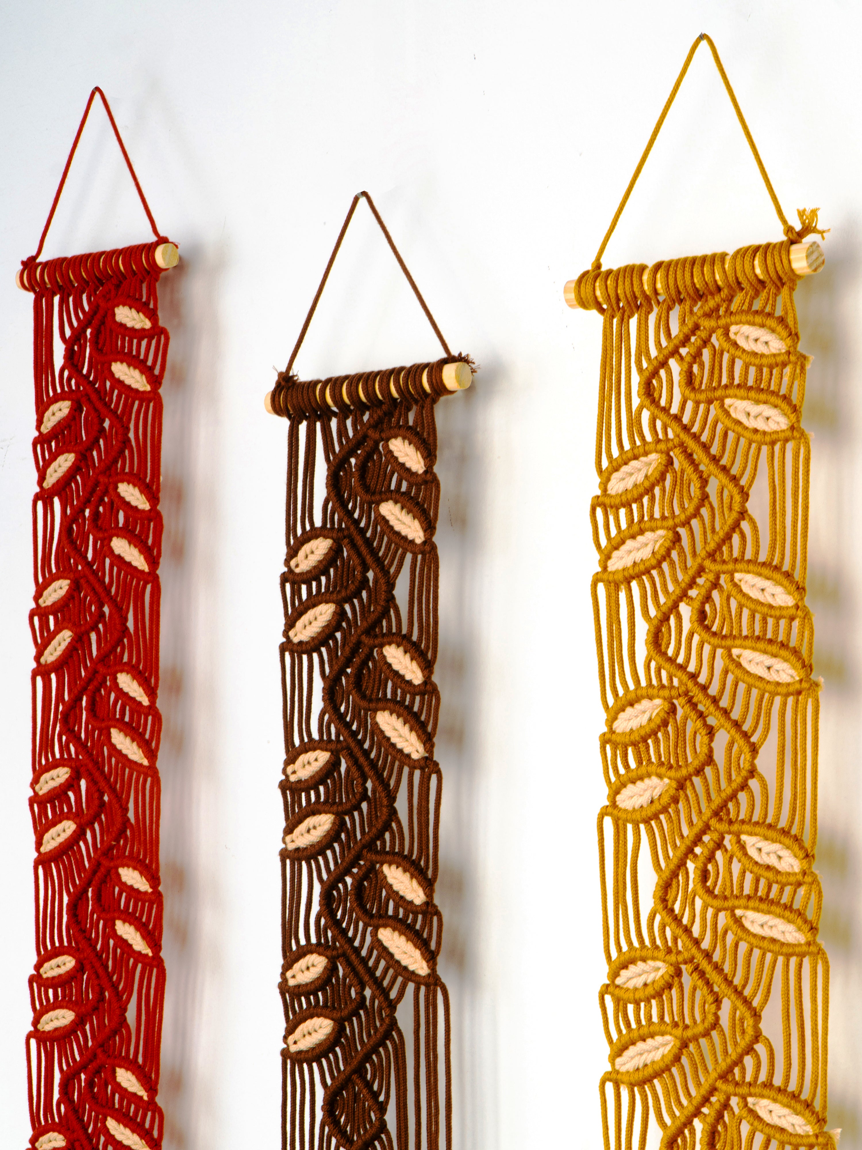 Three woven wall hangings in red, brown, and gold on a white background