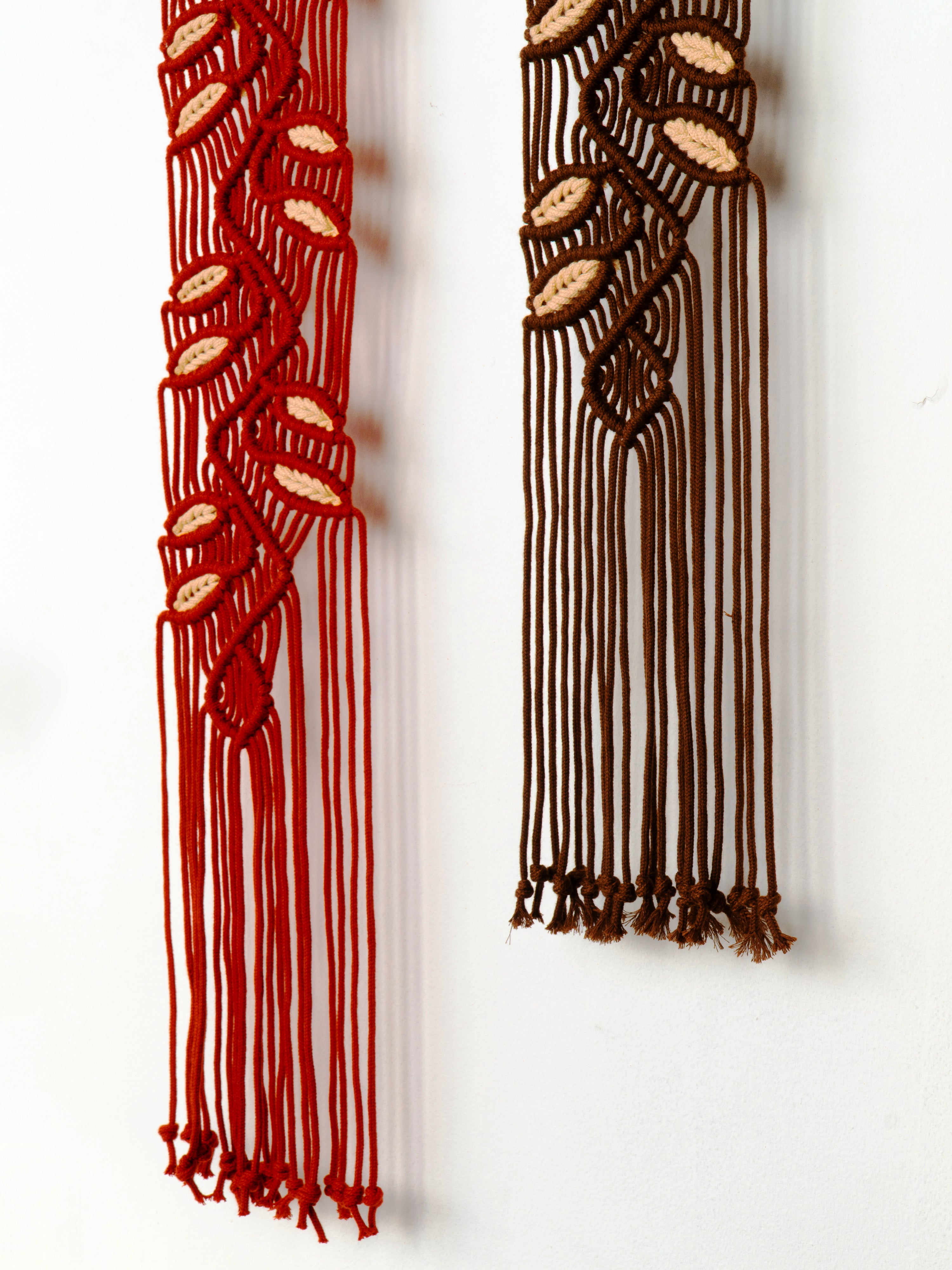 Two macrame wall hangings, one red and one brown, against a white background.