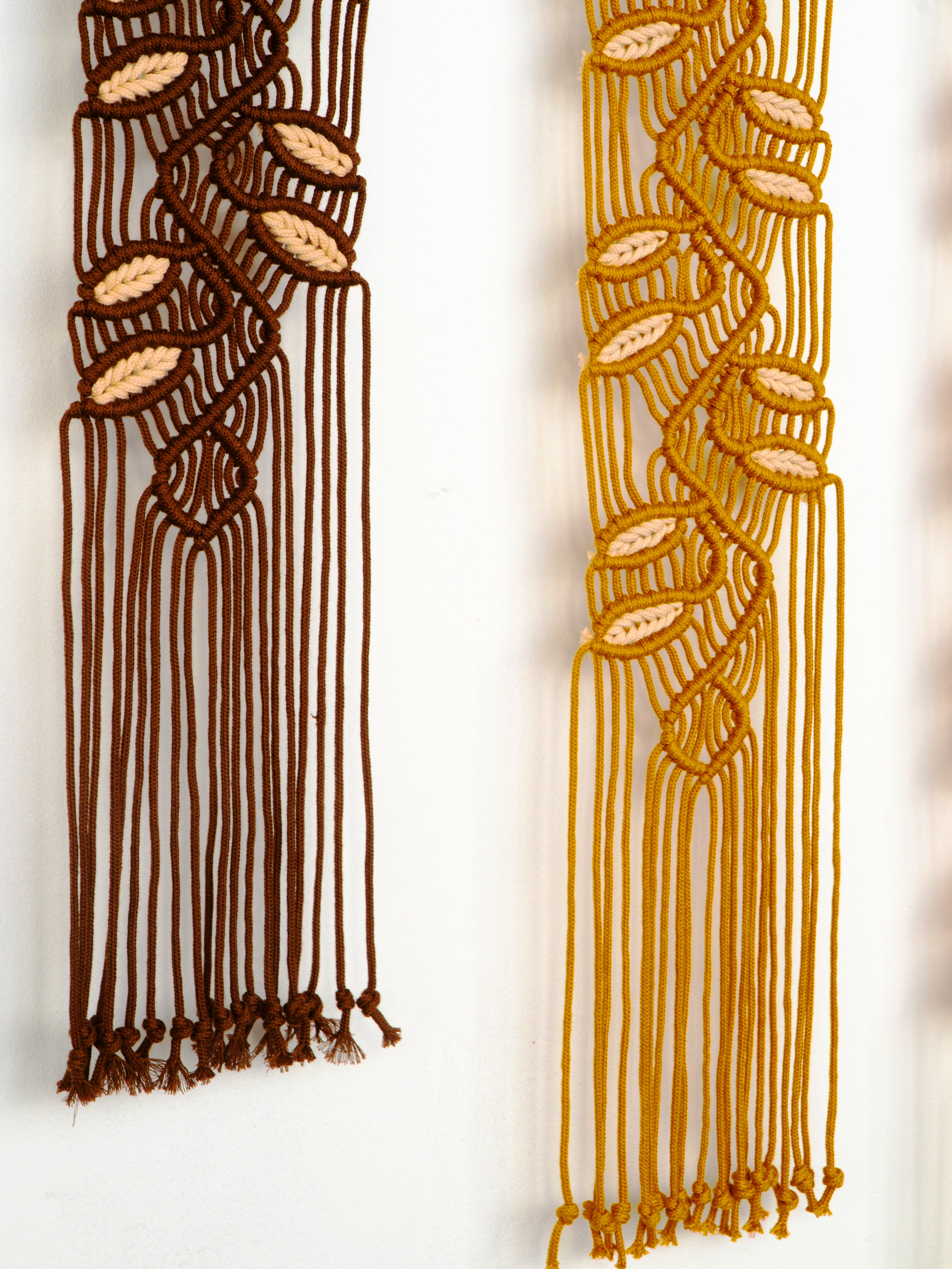 Two macrame wall hangings, one brown and one gold, on a white background.