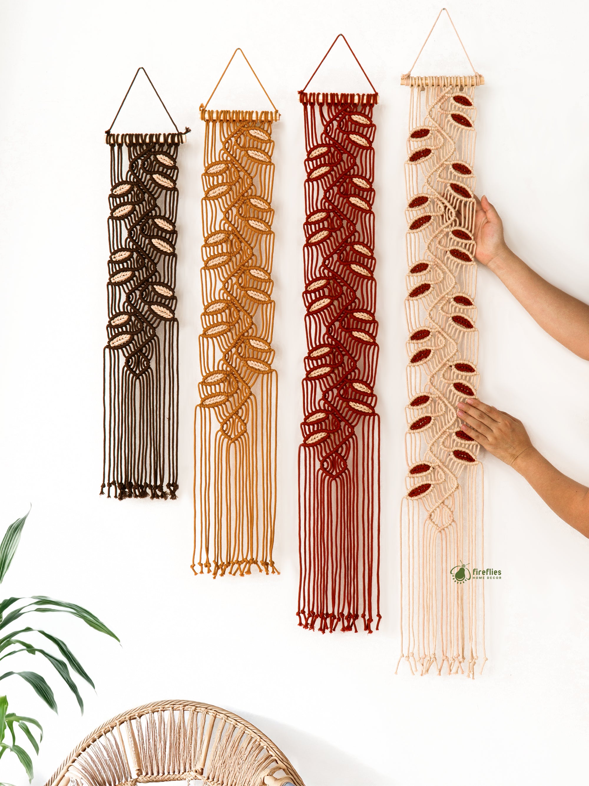 Set of four macrame wall hangings in different colors being arranged by a person.